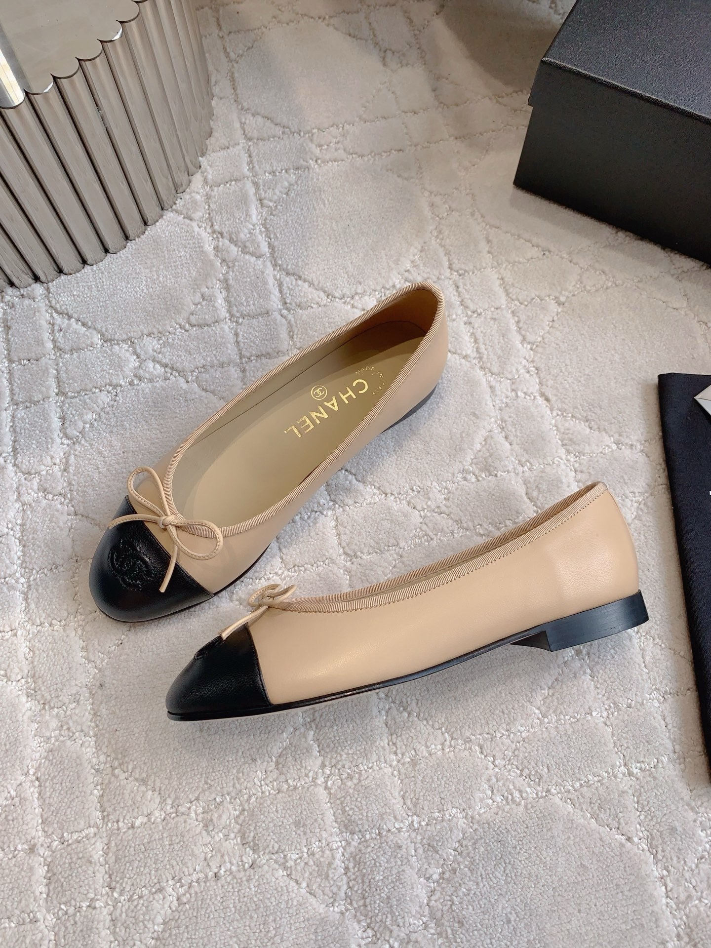 Classic Chanel beige lambskin ballerina flats with black toe caps and bow detail displayed on a marble surface. - Hình 4