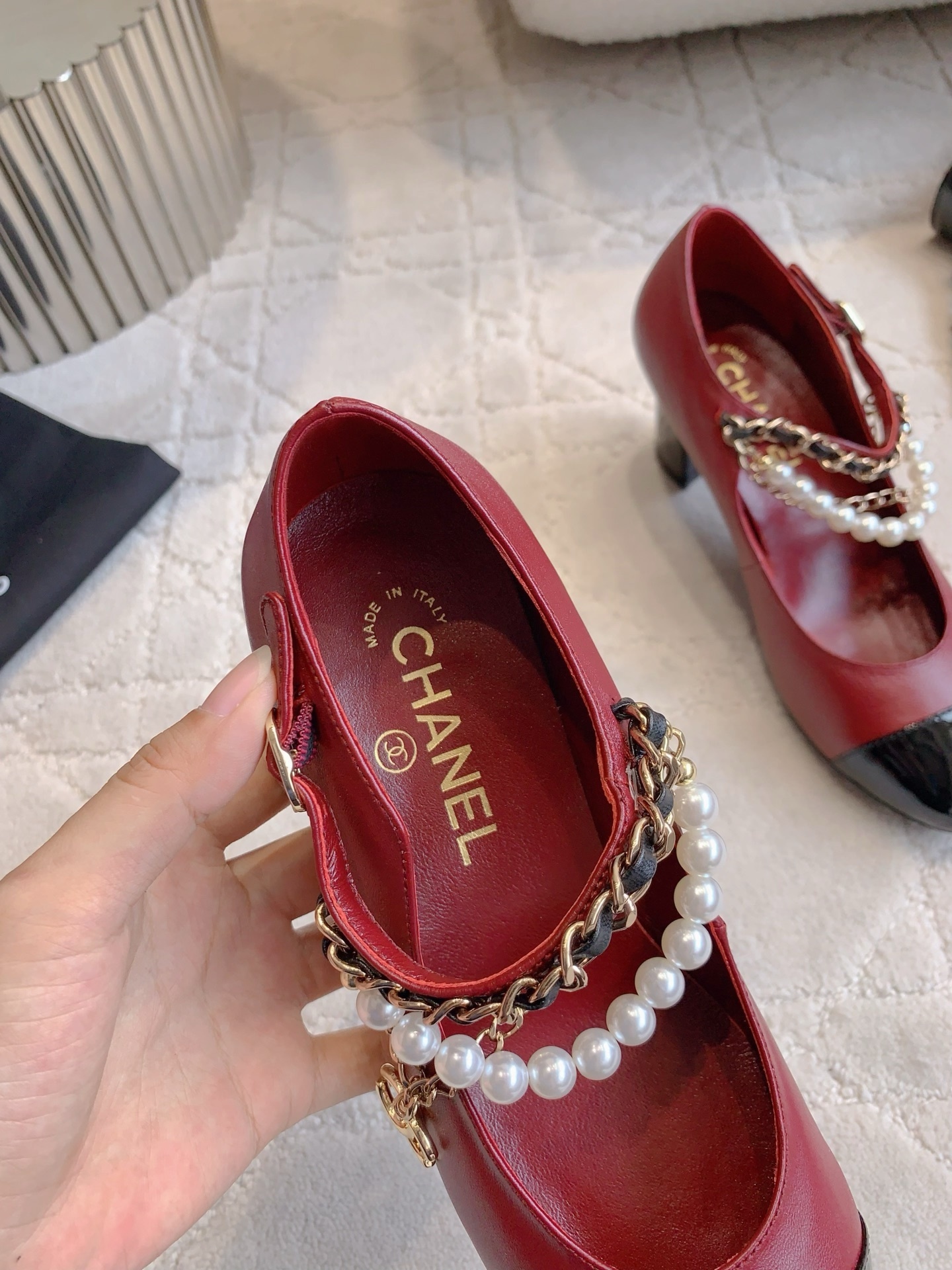 Luxury Chanel red leather Mary Jane pumps with black patent toe and decorative pearl chain strap on a marble table. - Hình 8