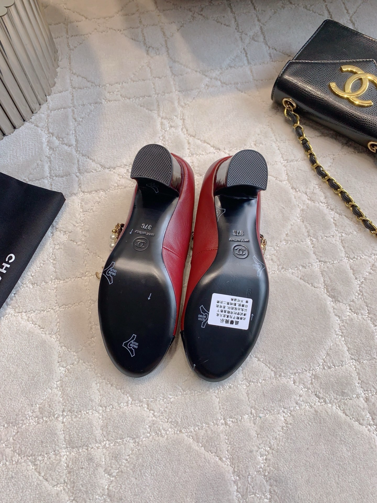 Luxury Chanel red leather Mary Jane pumps with black patent toe and decorative pearl chain strap on a marble table. - Hình 6