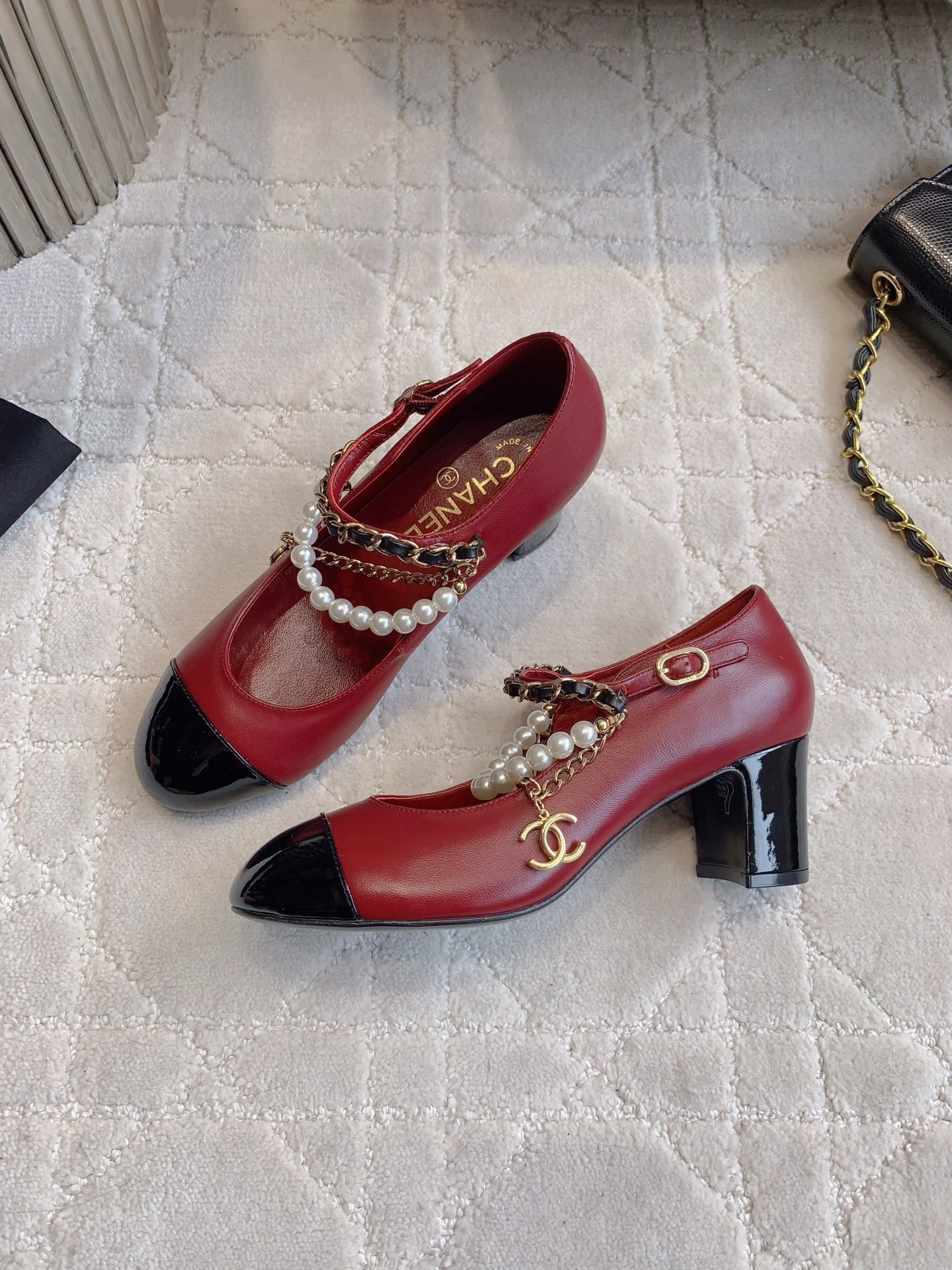Luxury Chanel red leather Mary Jane pumps with black patent toe and decorative pearl chain strap on a marble table. - Hình 4