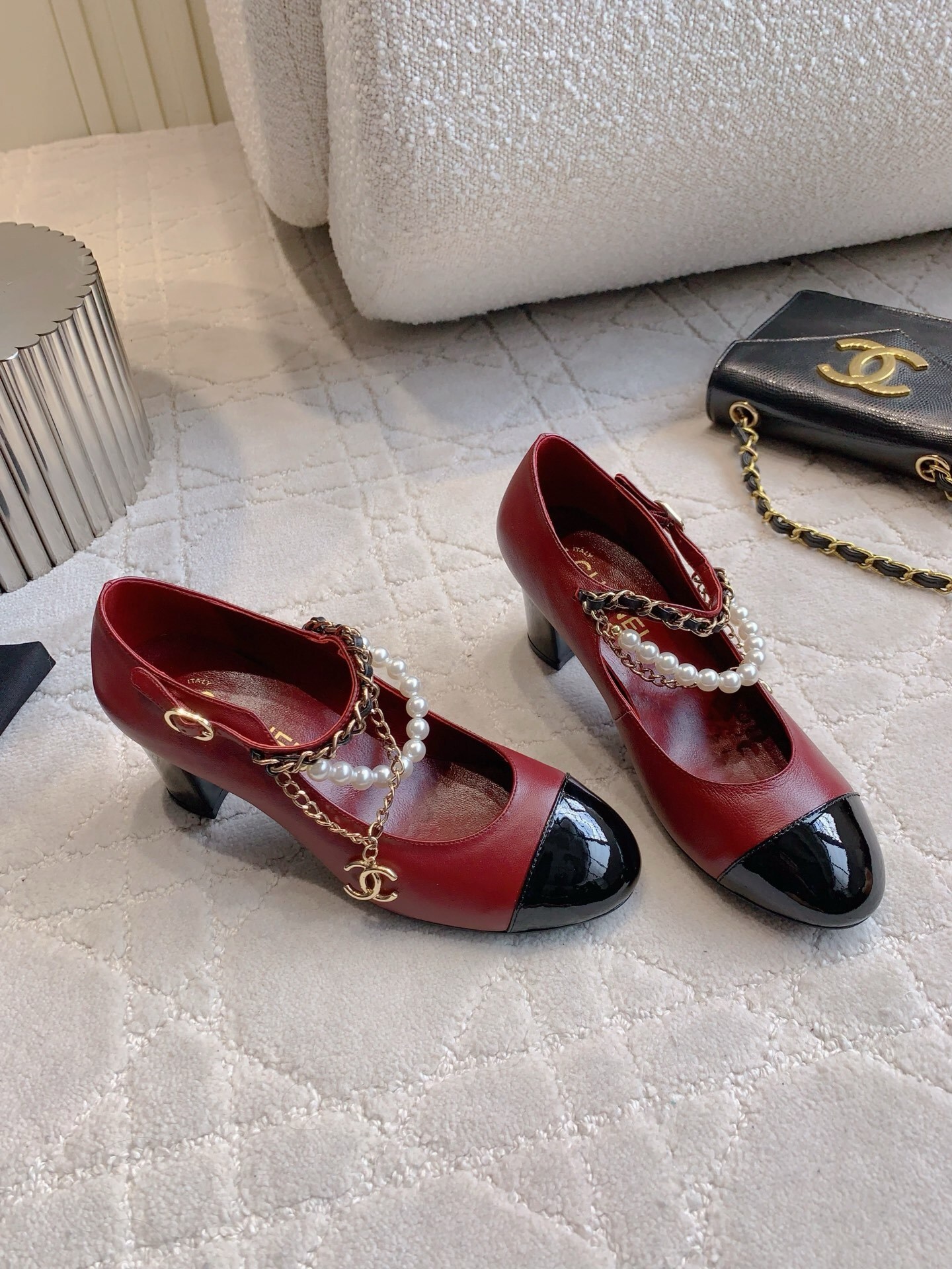 Luxury Chanel red leather Mary Jane pumps with black patent toe and decorative pearl chain strap on a marble table. - Hình 3