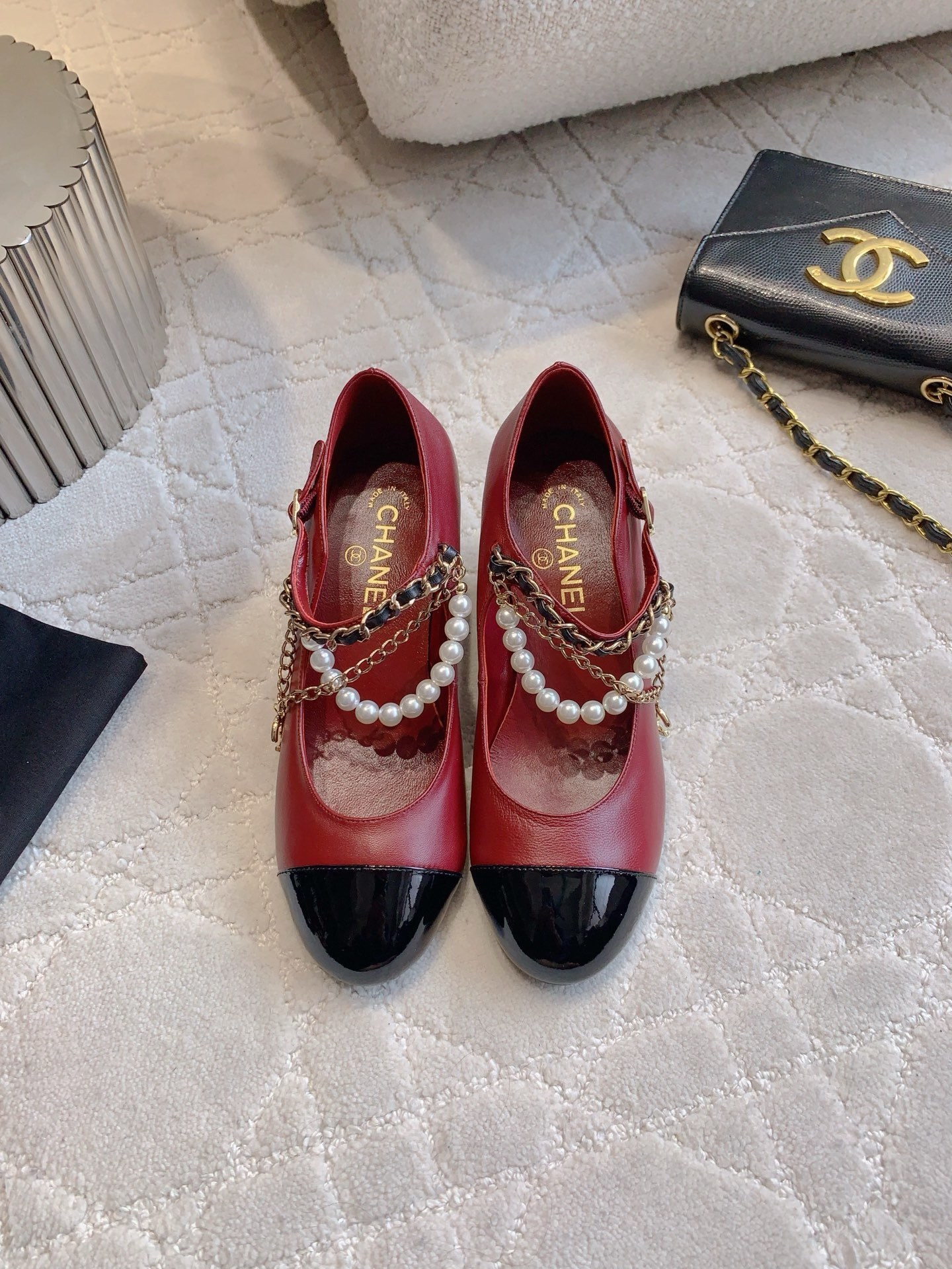 Luxury Chanel red leather Mary Jane pumps with black patent toe and decorative pearl chain strap on a marble table. - Hình 2