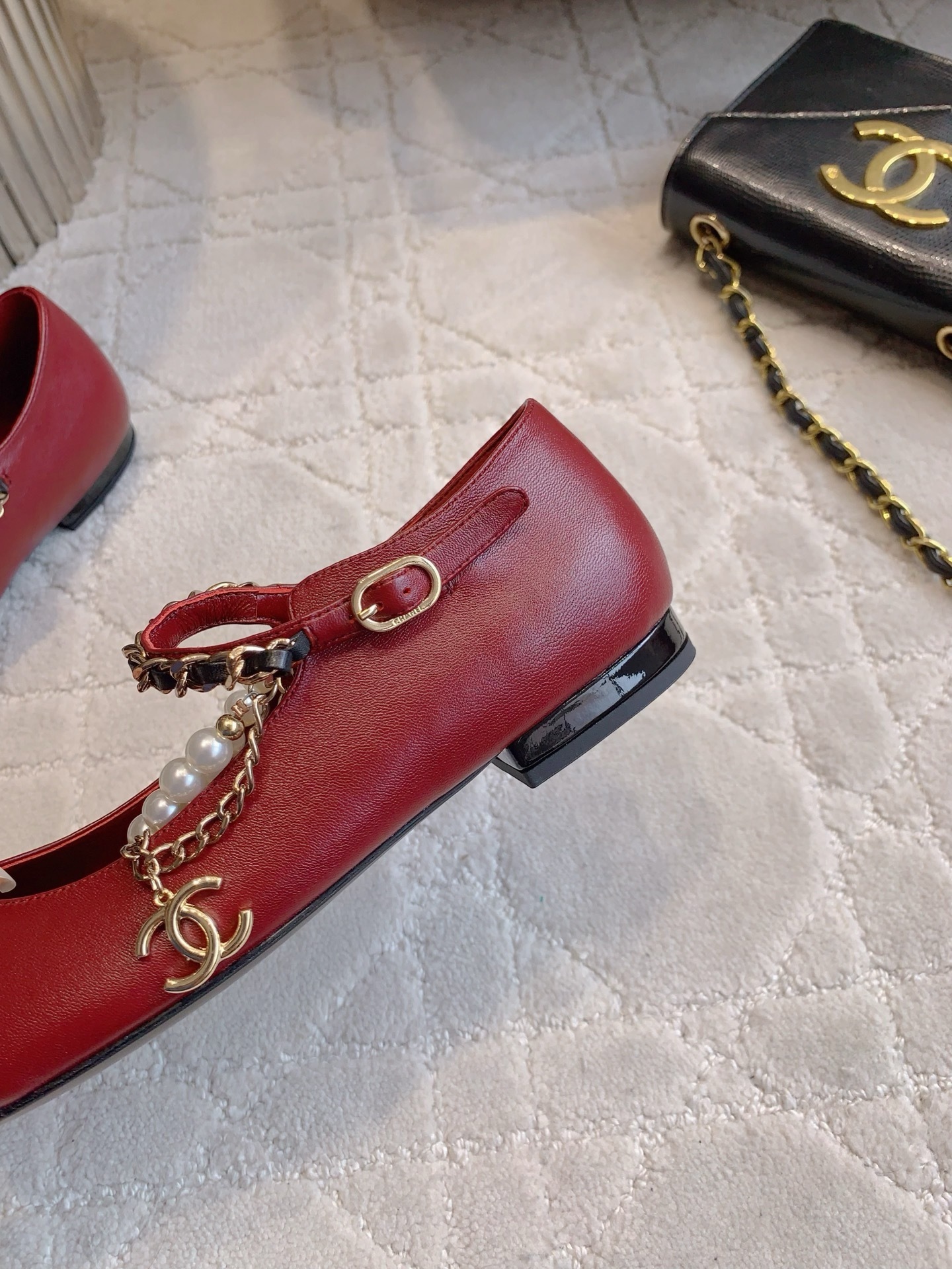 Chanel red leather ballet flats with black patent toe and pearl chain strap on a marble surface. - Hình 9