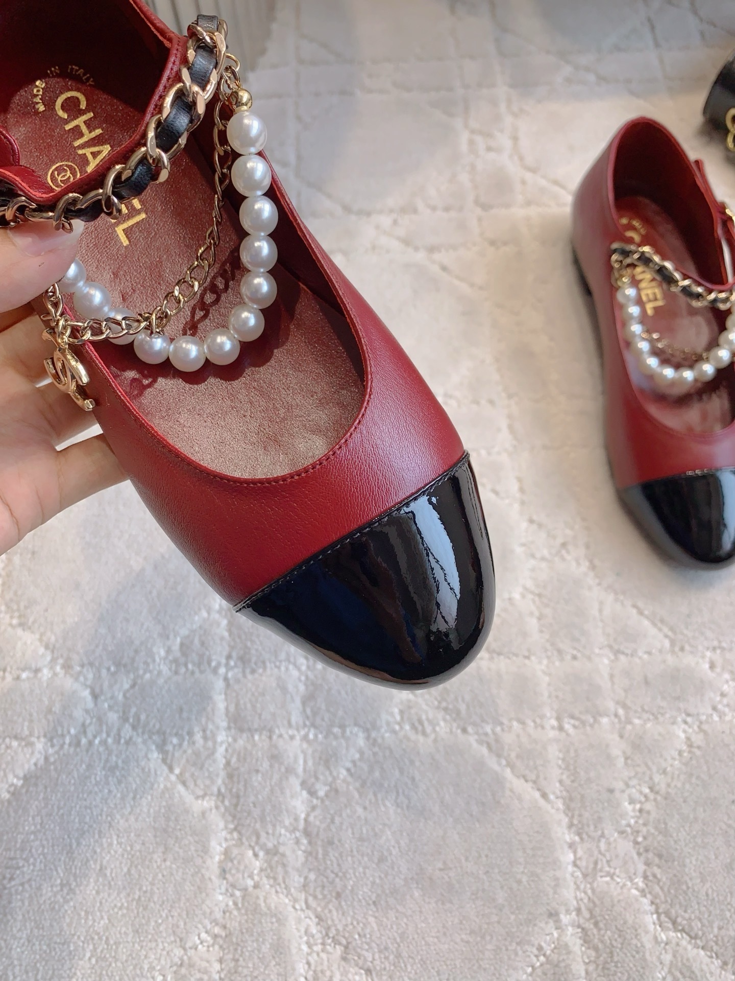 Chanel red leather ballet flats with black patent toe and pearl chain strap on a marble surface. - Hình 7