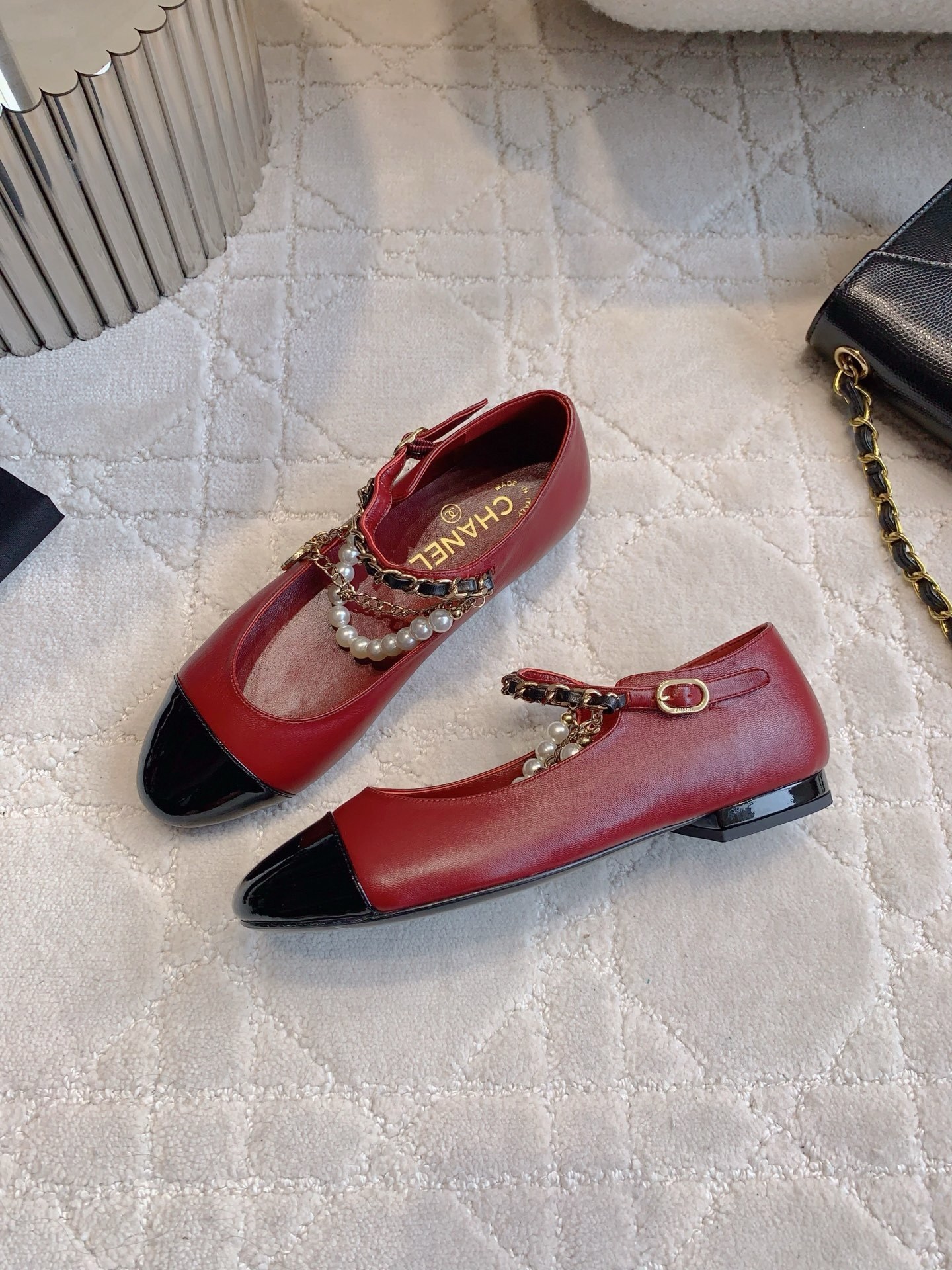 Chanel red leather ballet flats with black patent toe and pearl chain strap on a marble surface. - Hình 4
