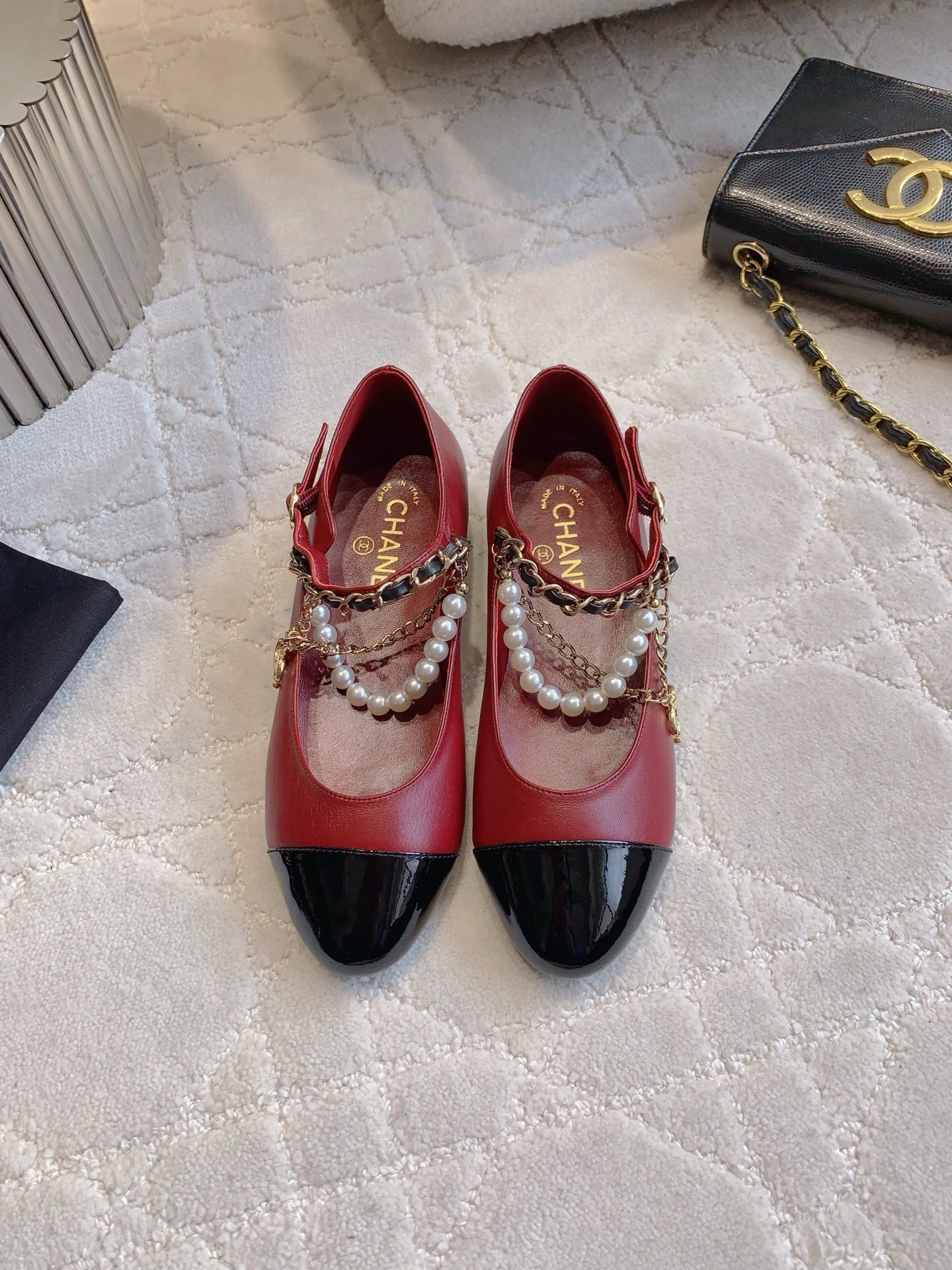 Chanel red leather ballet flats with black patent toe and pearl chain strap on a marble surface. - Hình 2