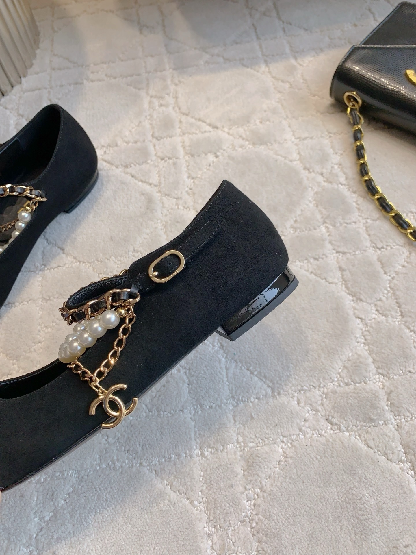 Pair of black Chanel Mary Jane flats with suede body, patent leather cap toe, and gold chain pearl straps on a marble table. - Hình 9