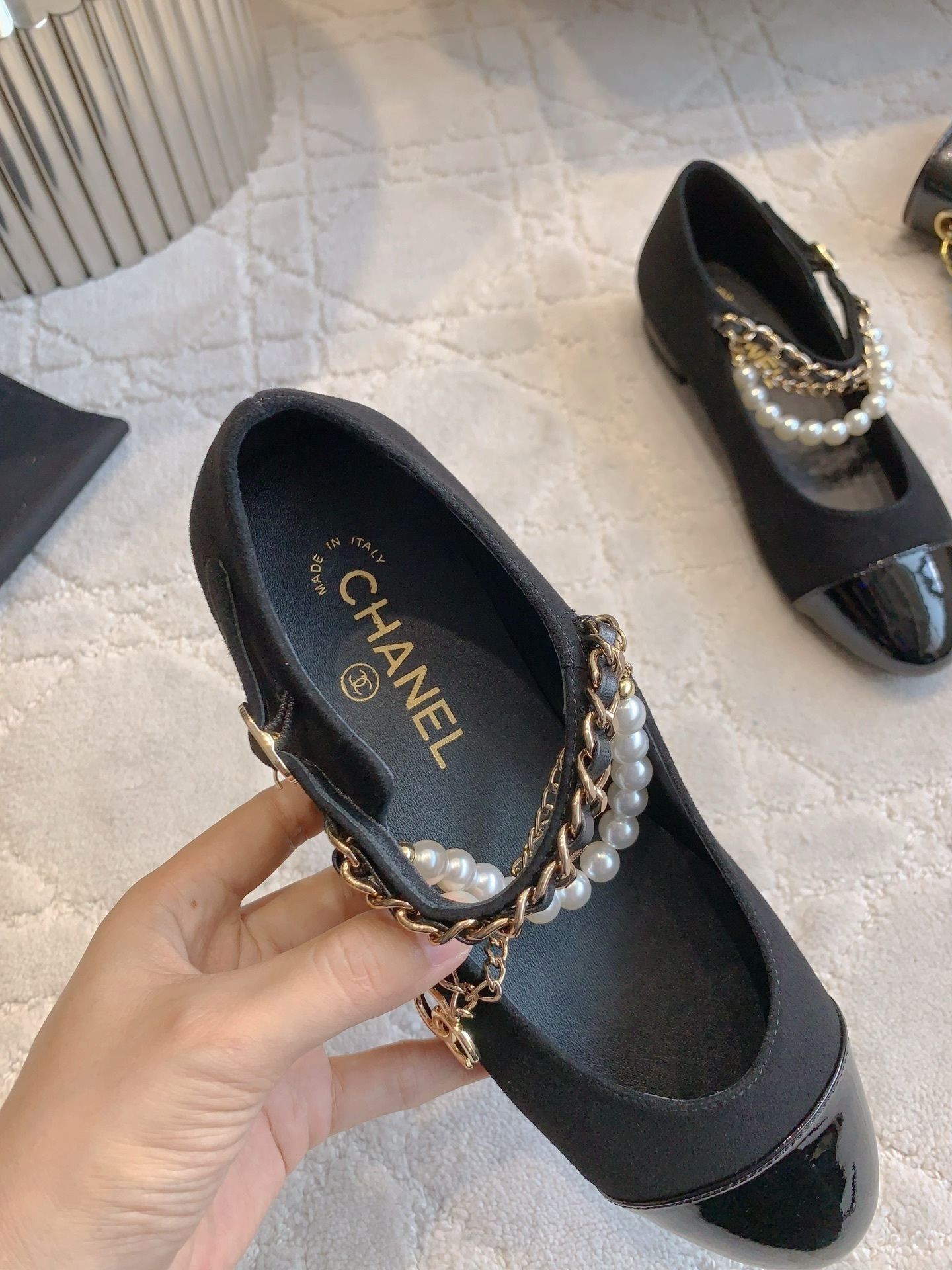 Pair of black Chanel Mary Jane flats with suede body, patent leather cap toe, and gold chain pearl straps on a marble table. - Hình 8