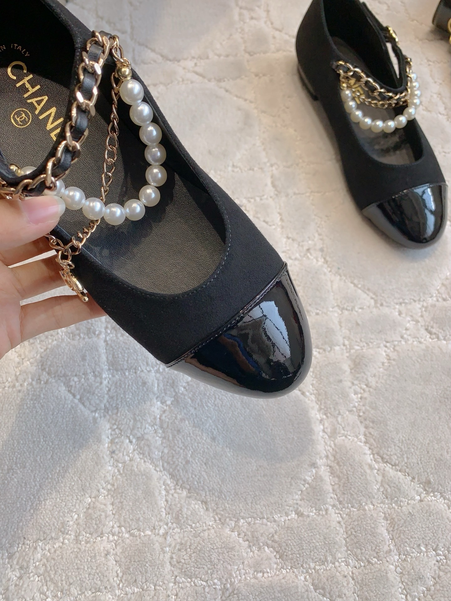 Pair of black Chanel Mary Jane flats with suede body, patent leather cap toe, and gold chain pearl straps on a marble table. - Hình 7
