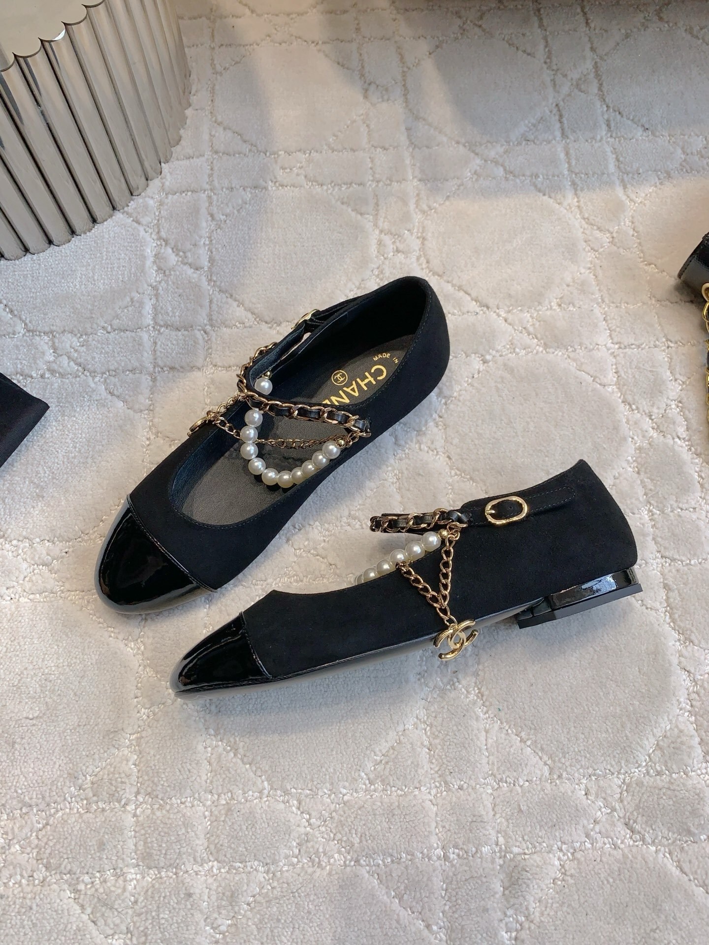 Pair of black Chanel Mary Jane flats with suede body, patent leather cap toe, and gold chain pearl straps on a marble table. - Hình 4