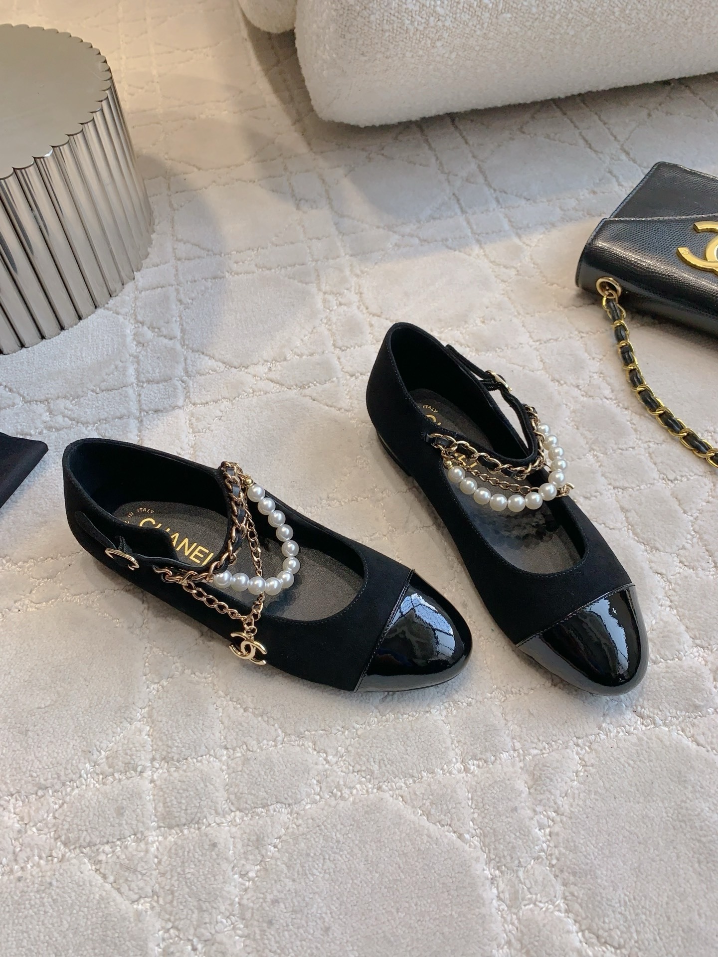 Pair of black Chanel Mary Jane flats with suede body, patent leather cap toe, and gold chain pearl straps on a marble table. - Hình 3