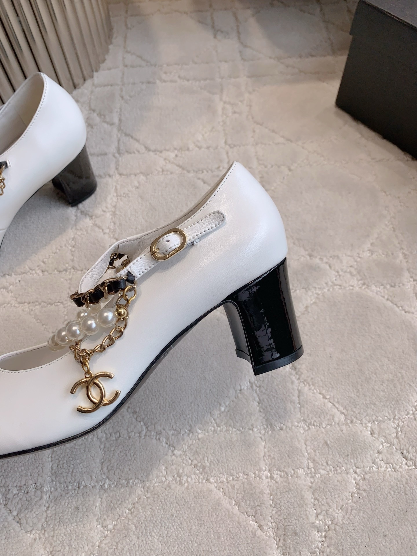 Luxury Chanel white and black Mary Jane pumps with pearl strands and gold chain details on a marble table - Hình 9