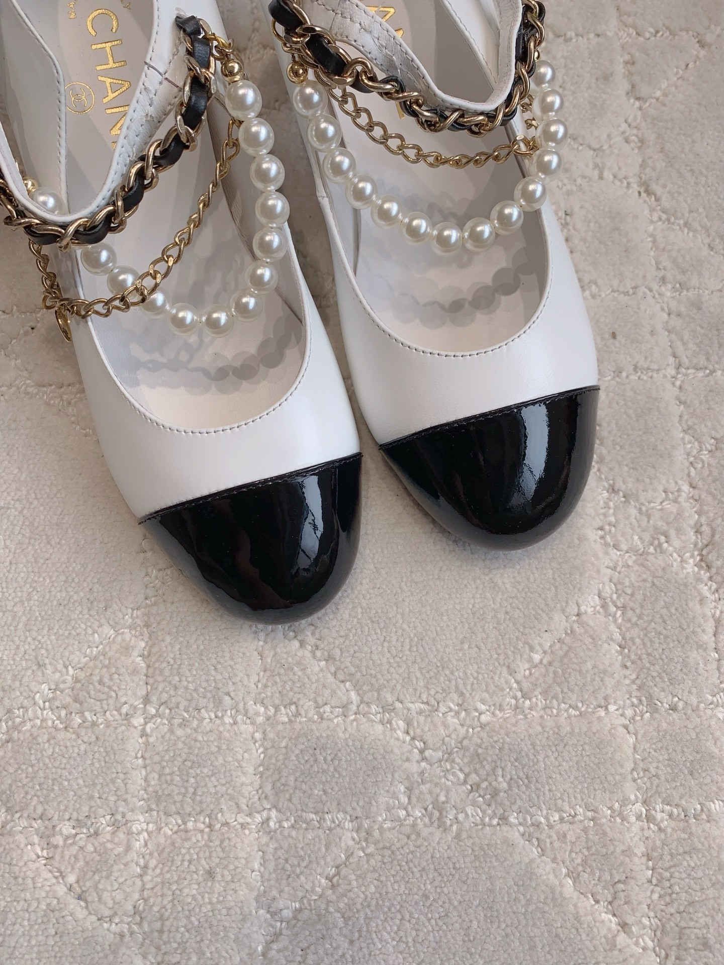 Luxury Chanel white and black Mary Jane pumps with pearl strands and gold chain details on a marble table - Hình 8