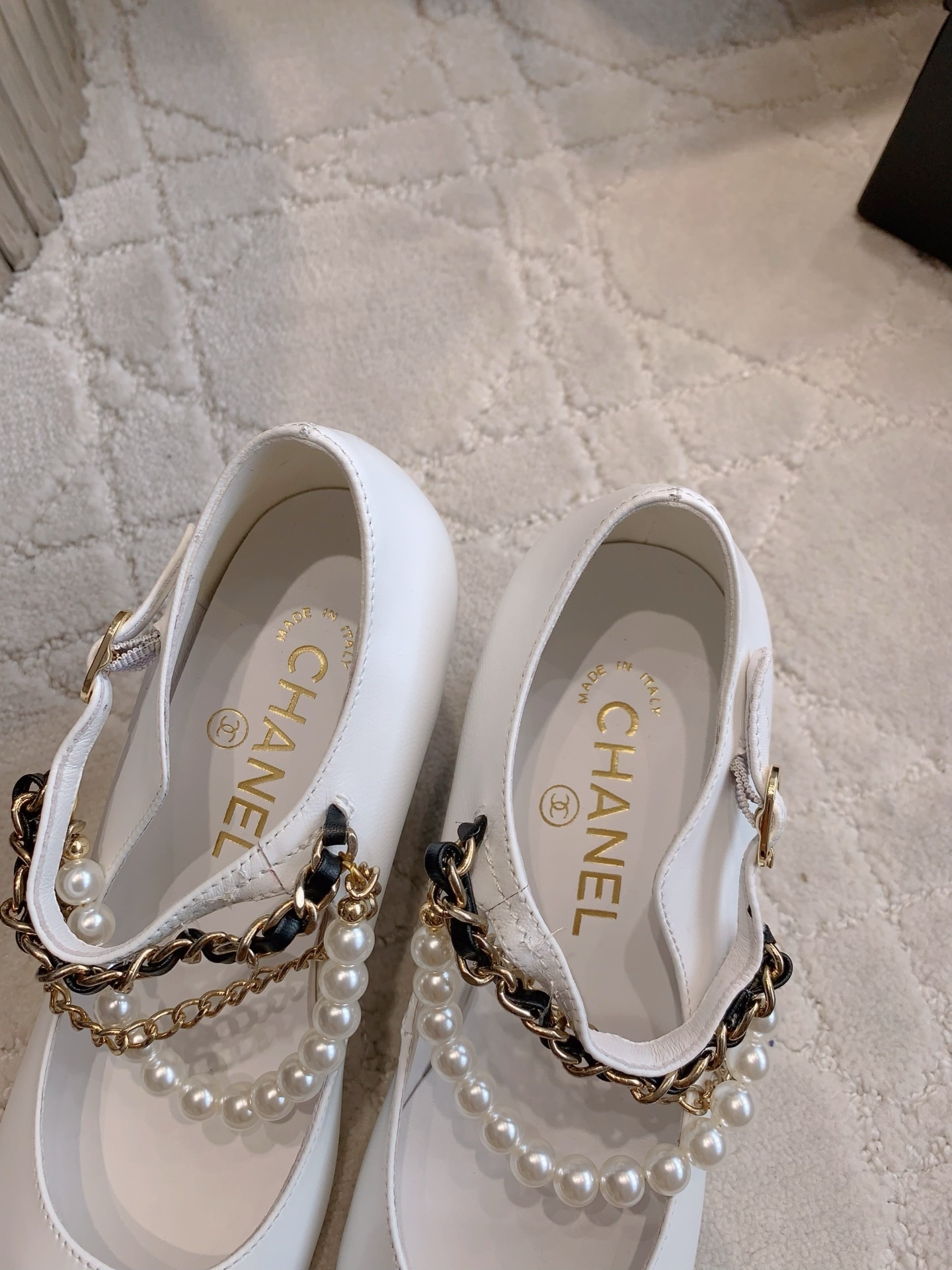 Luxury Chanel white and black Mary Jane pumps with pearl strands and gold chain details on a marble table - Hình 7