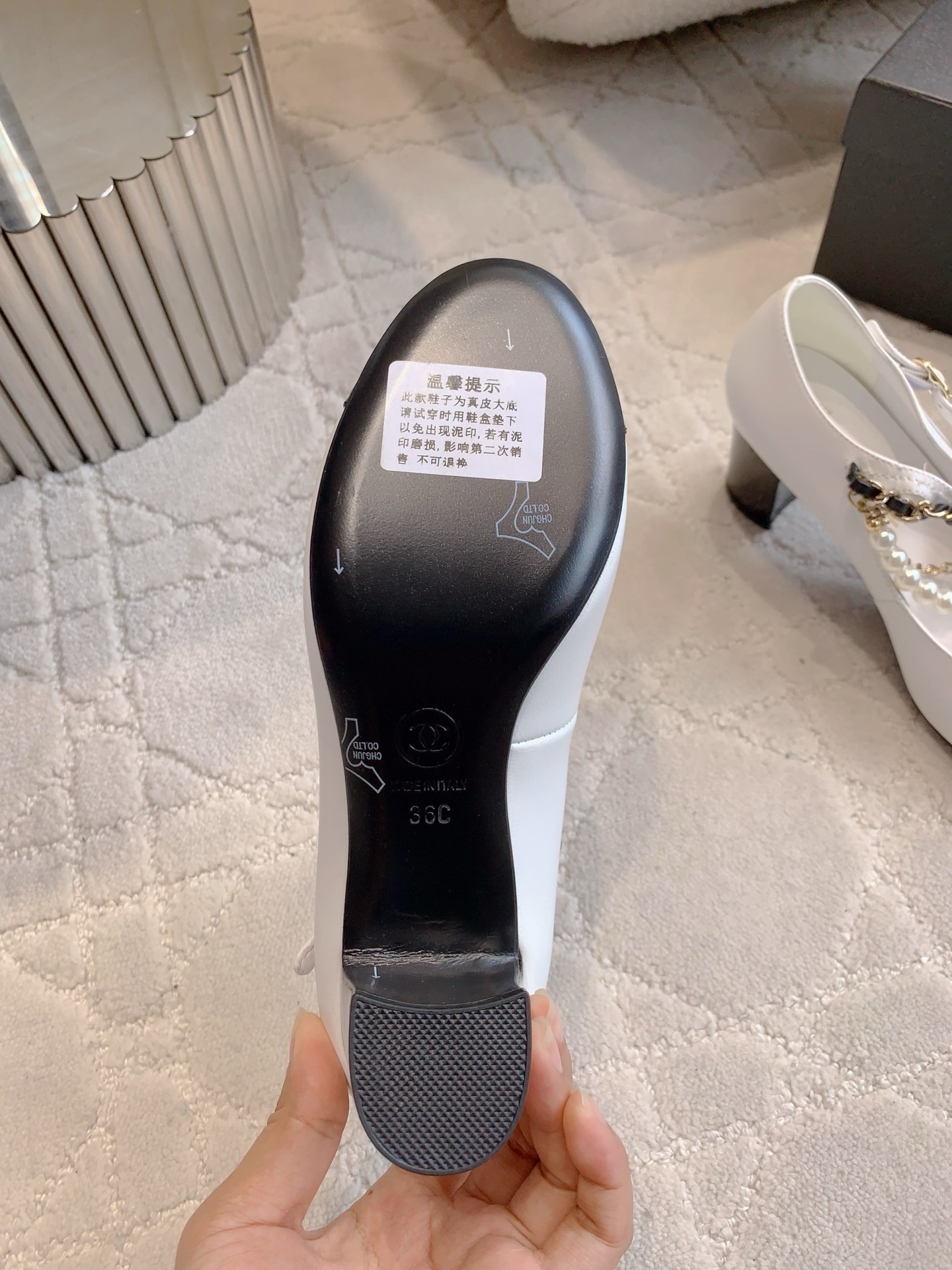 Luxury Chanel white and black Mary Jane pumps with pearl strands and gold chain details on a marble table - Hình 6