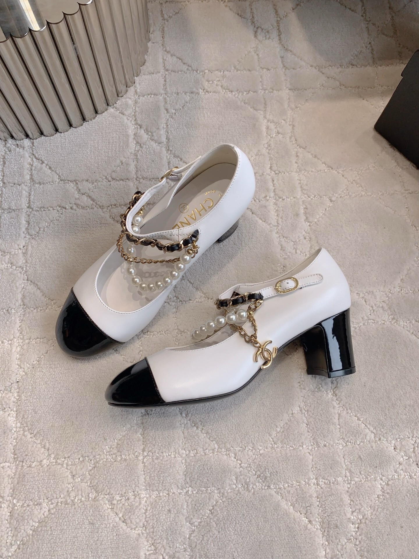 Luxury Chanel white and black Mary Jane pumps with pearl strands and gold chain details on a marble table - Hình 4