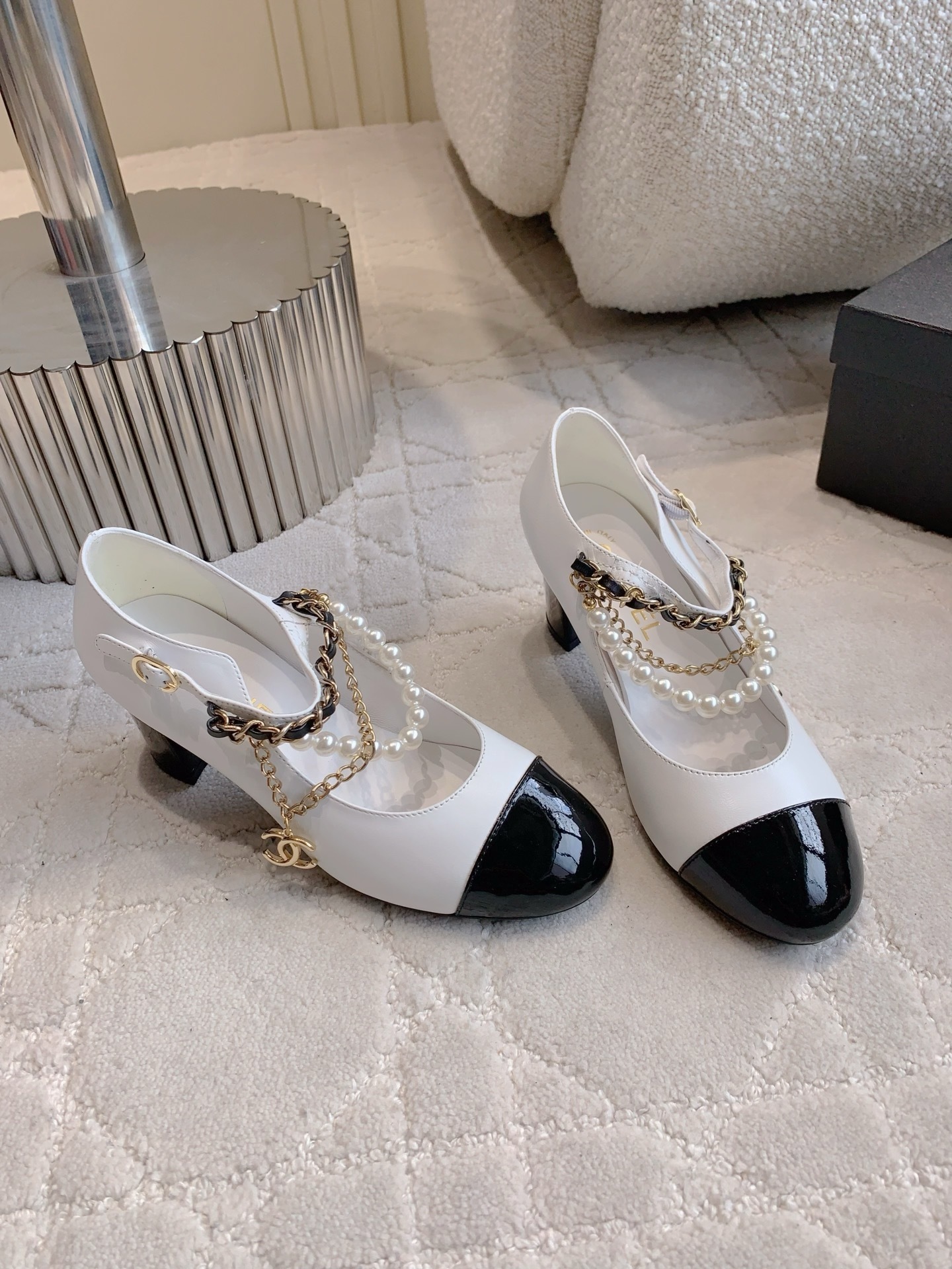 Luxury Chanel white and black Mary Jane pumps with pearl strands and gold chain details on a marble table - Hình 3