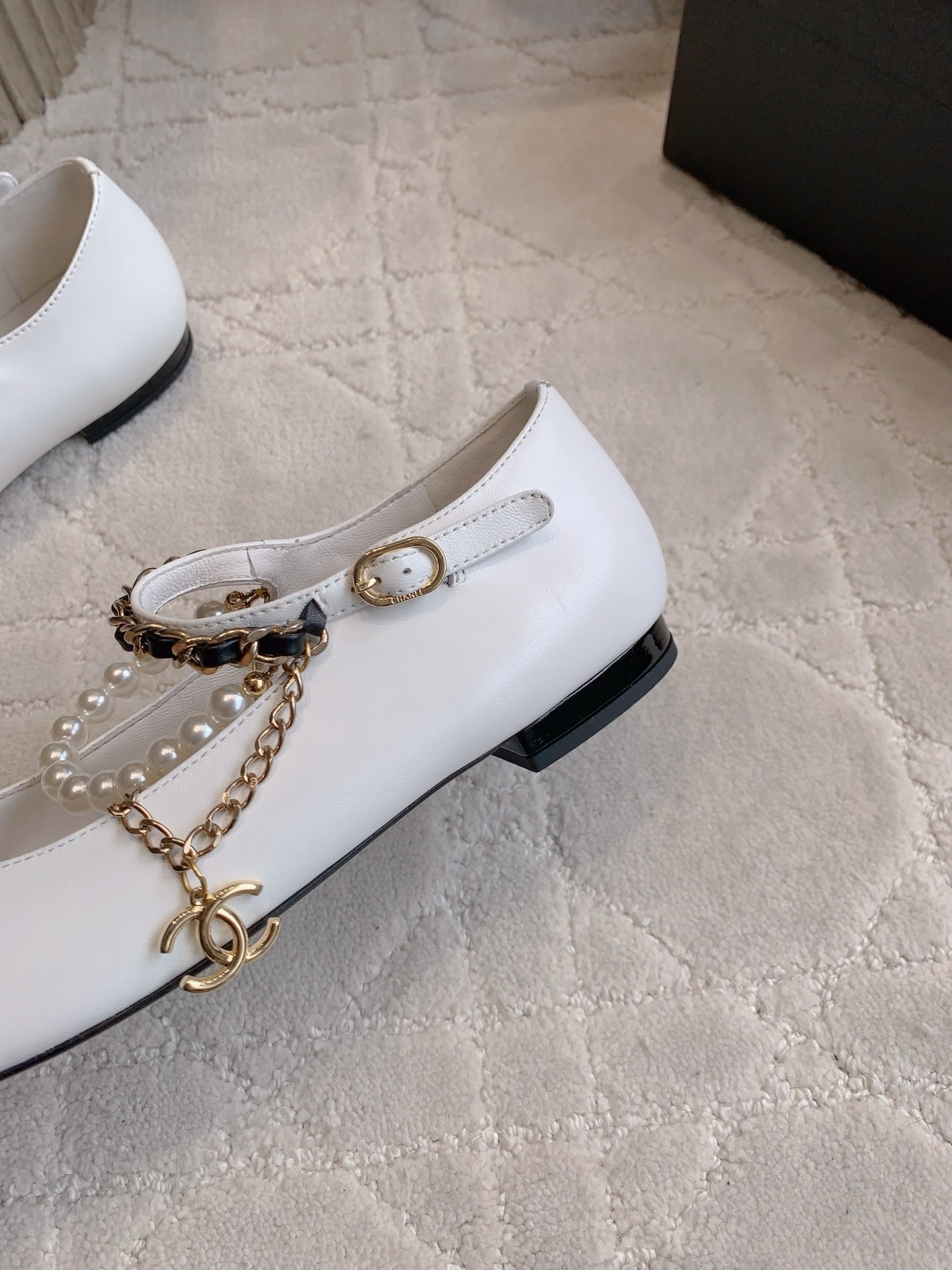 Elegant white leather ballet flats with black patent cap toe and decorative pearl and gold chain strap on a marble surface - Hình 9