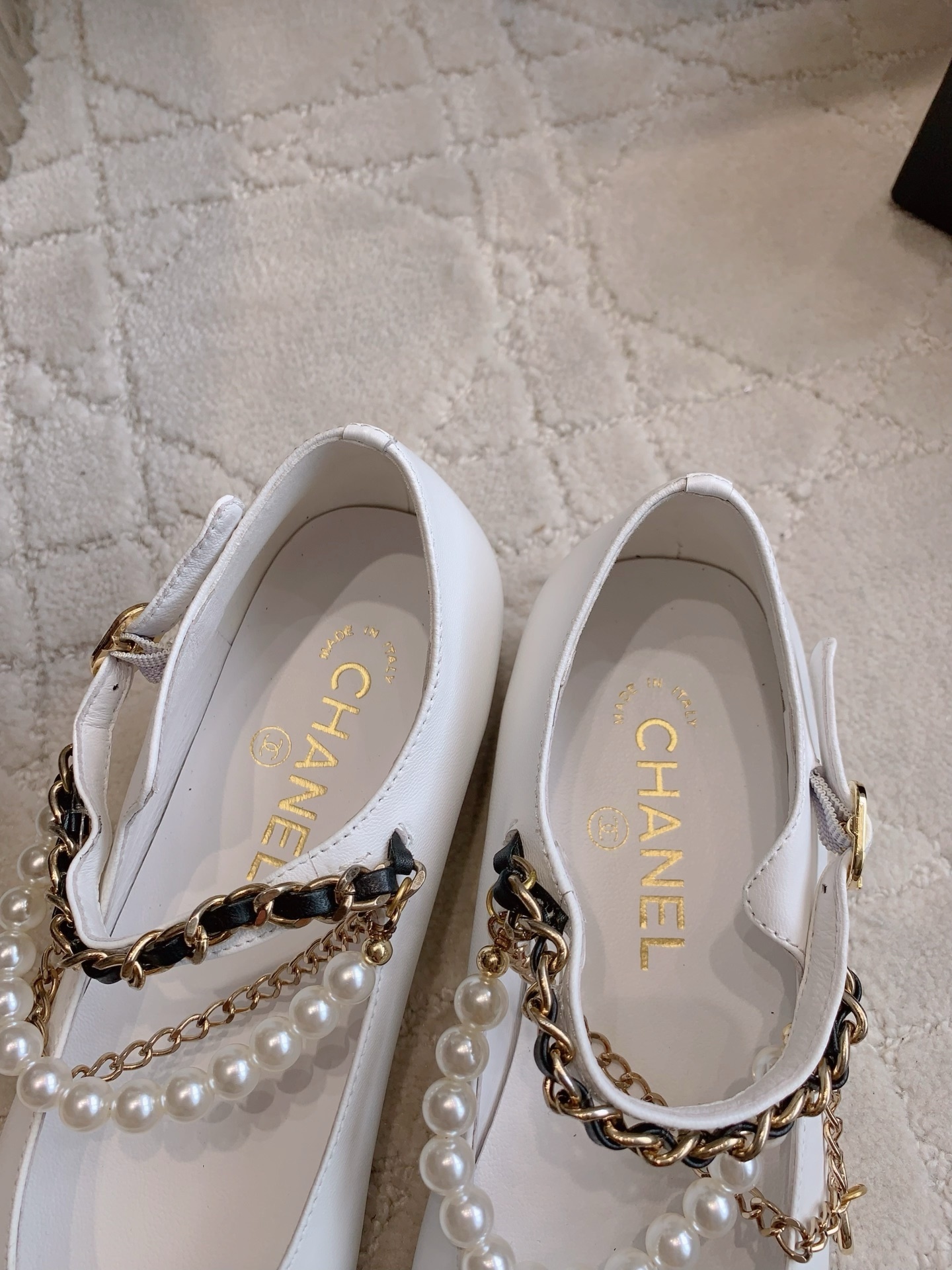 Elegant white leather ballet flats with black patent cap toe and decorative pearl and gold chain strap on a marble surface - Hình 8