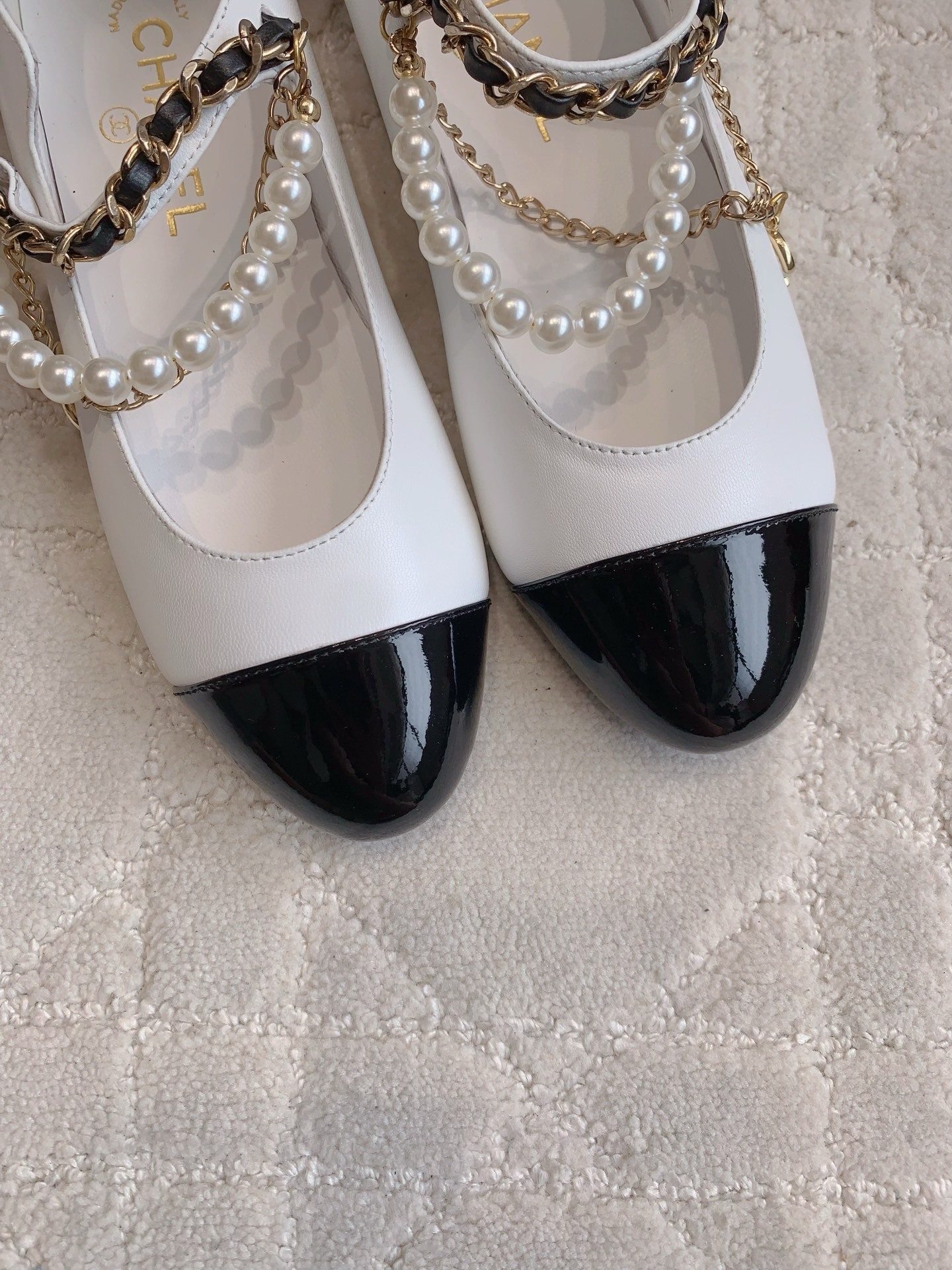 Elegant white leather ballet flats with black patent cap toe and decorative pearl and gold chain strap on a marble surface - Hình 7