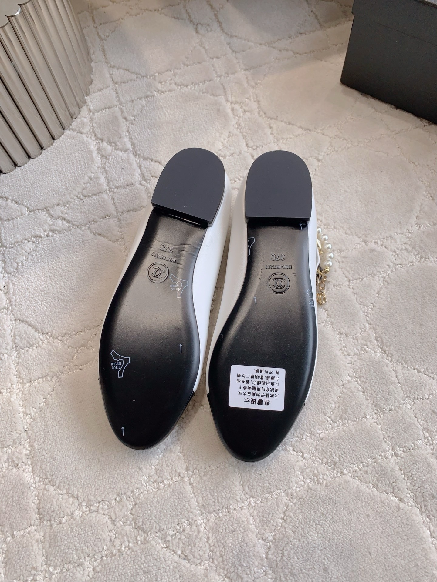 Elegant white leather ballet flats with black patent cap toe and decorative pearl and gold chain strap on a marble surface - Hình 6