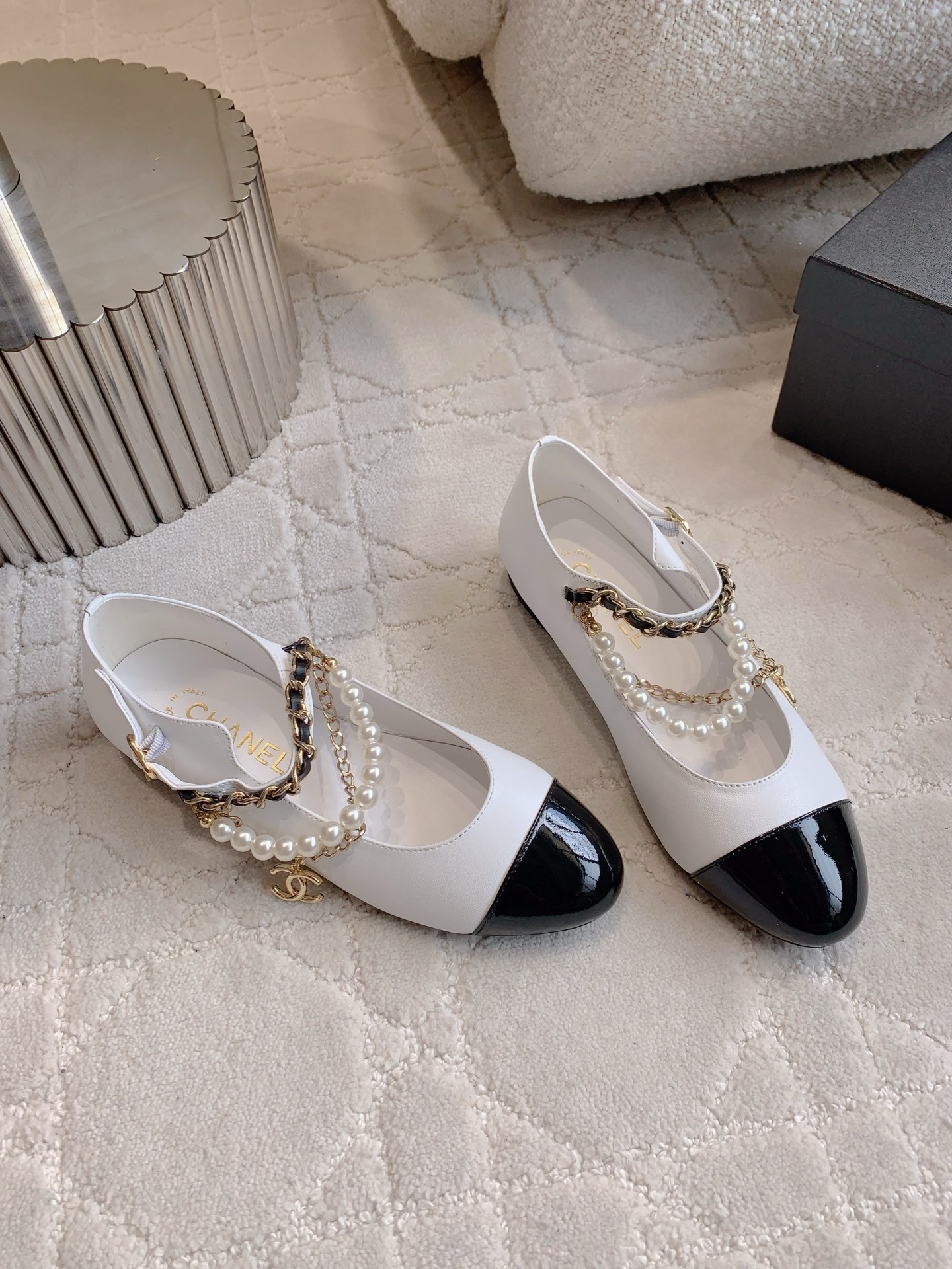 Elegant white leather ballet flats with black patent cap toe and decorative pearl and gold chain strap on a marble surface - Hình 3