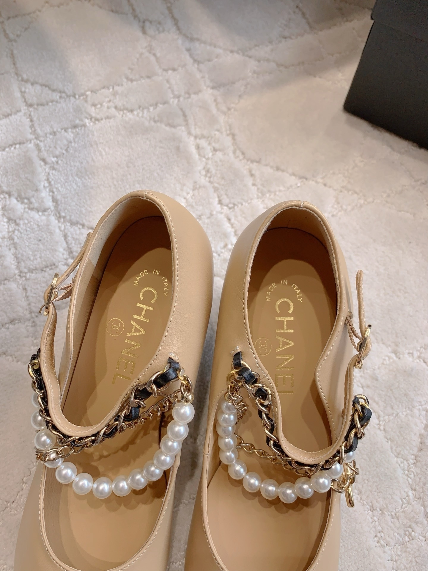 Chanel two-tone beige and black leather Mary Jane pumps with pearl and gold chain details on a marble table - Hình 8