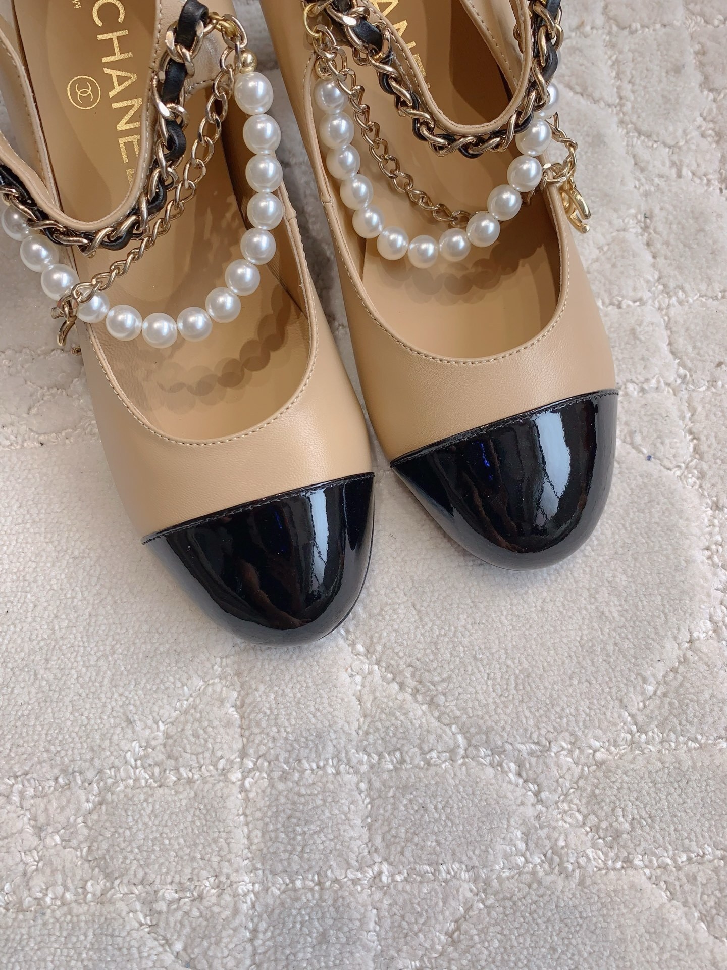Chanel two-tone beige and black leather Mary Jane pumps with pearl and gold chain details on a marble table - Hình 7