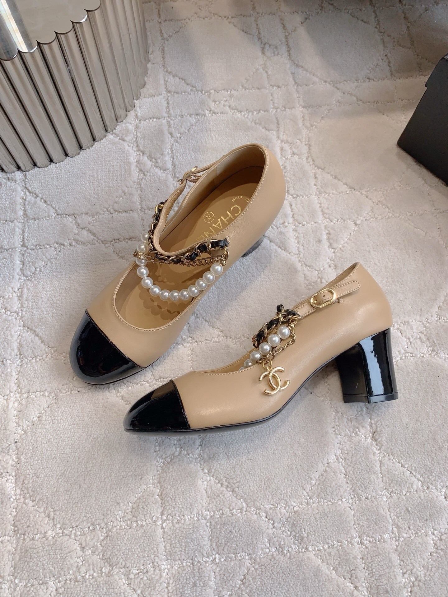 Chanel two-tone beige and black leather Mary Jane pumps with pearl and gold chain details on a marble table - Hình 4