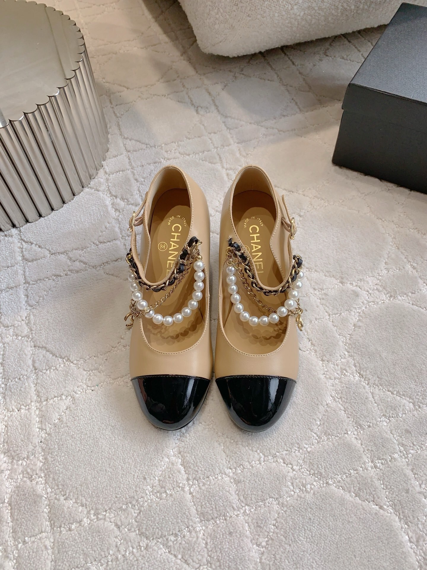 Chanel two-tone beige and black leather Mary Jane pumps with pearl and gold chain details on a marble table - Hình 2