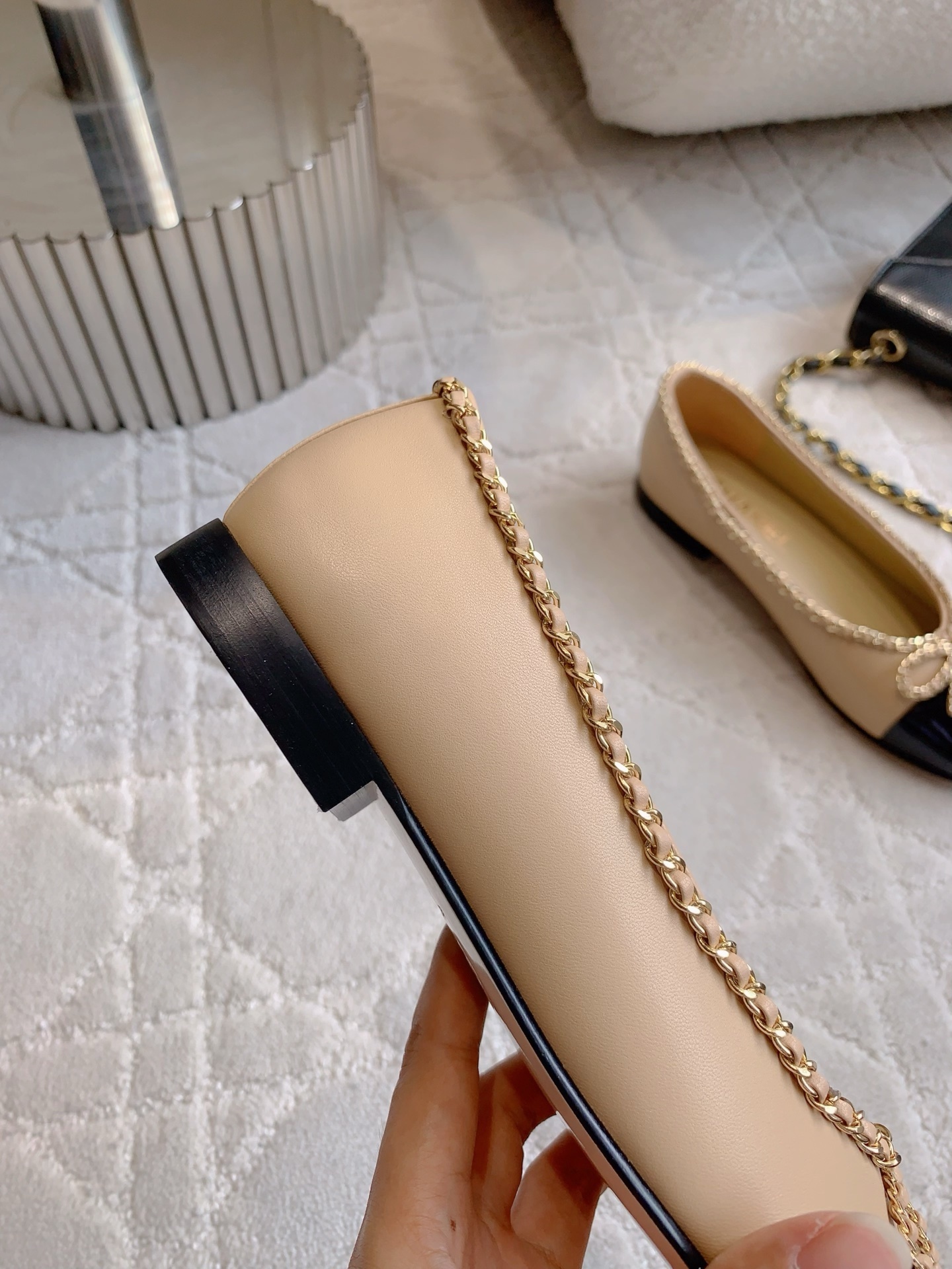 Luxury Chanel beige leather ballerina flats with black patent leather cap toe and gold chain trim detail displayed on a marble surface - Hình 9