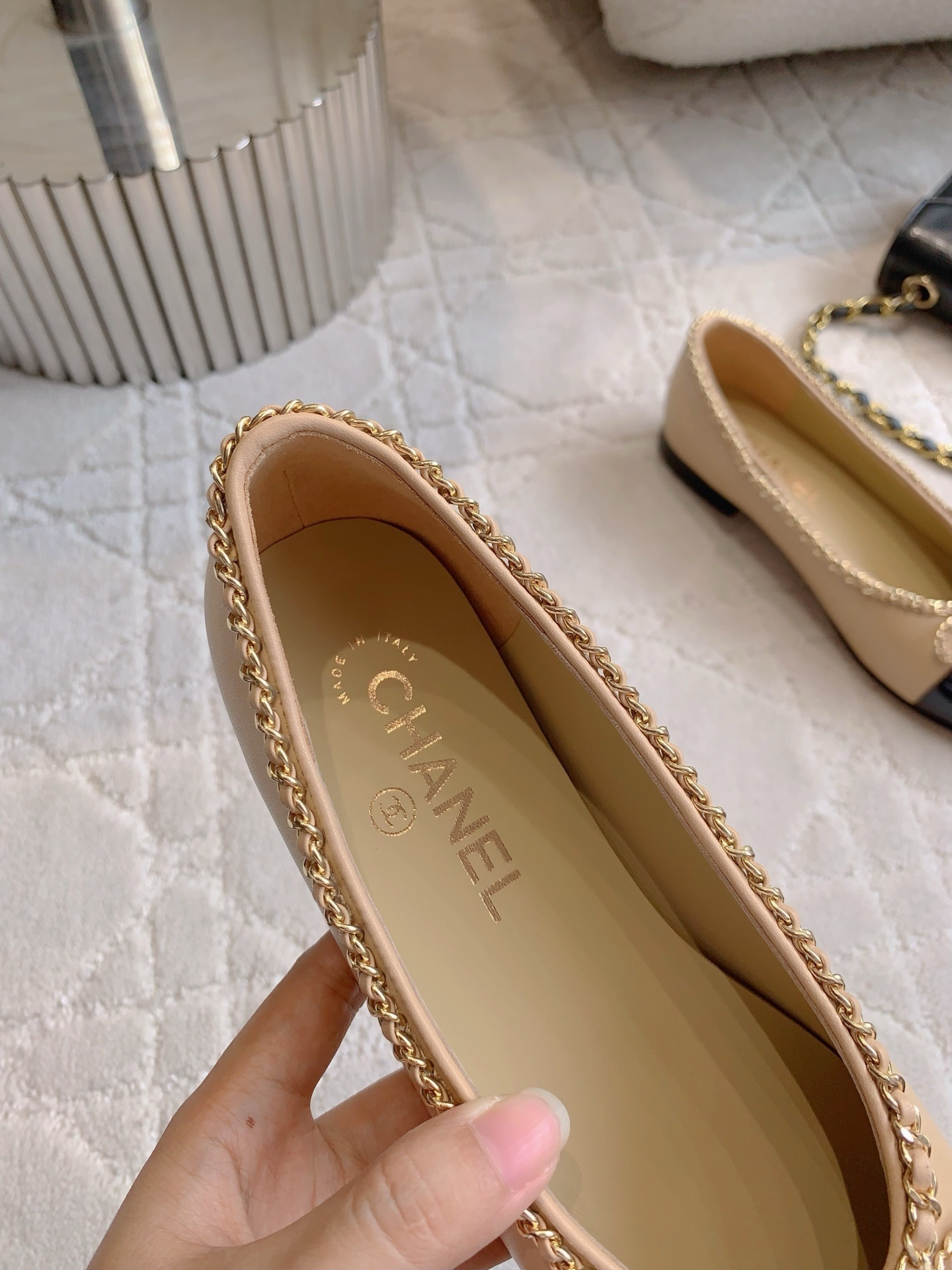 Luxury Chanel beige leather ballerina flats with black patent leather cap toe and gold chain trim detail displayed on a marble surface - Hình 8