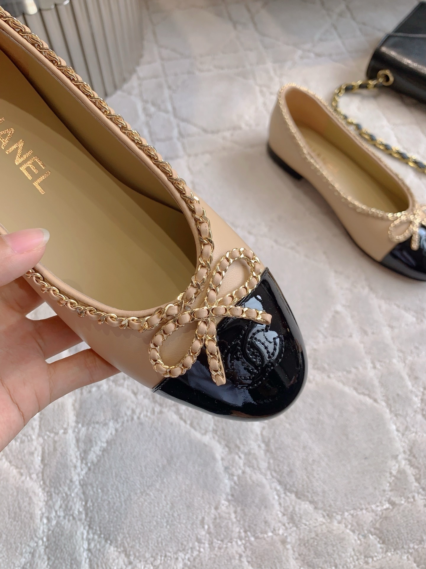 Luxury Chanel beige leather ballerina flats with black patent leather cap toe and gold chain trim detail displayed on a marble surface - Hình 7