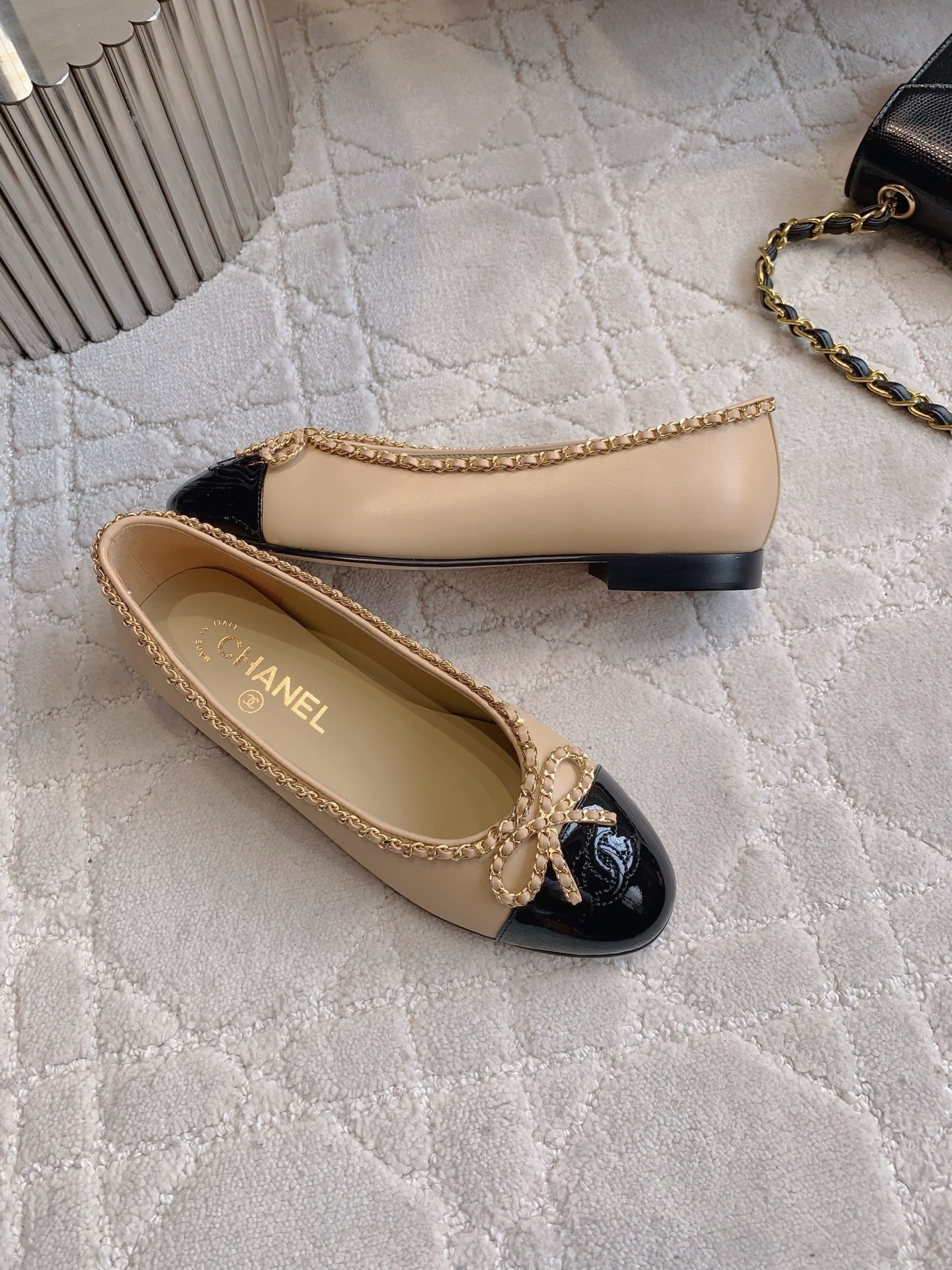 Luxury Chanel beige leather ballerina flats with black patent leather cap toe and gold chain trim detail displayed on a marble surface - Hình 4