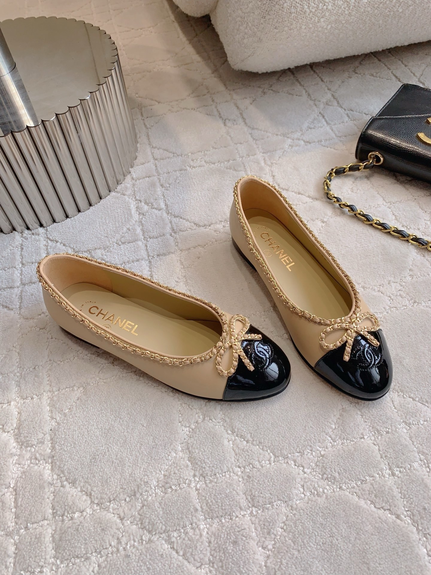 Luxury Chanel beige leather ballerina flats with black patent leather cap toe and gold chain trim detail displayed on a marble surface - Hình 3
