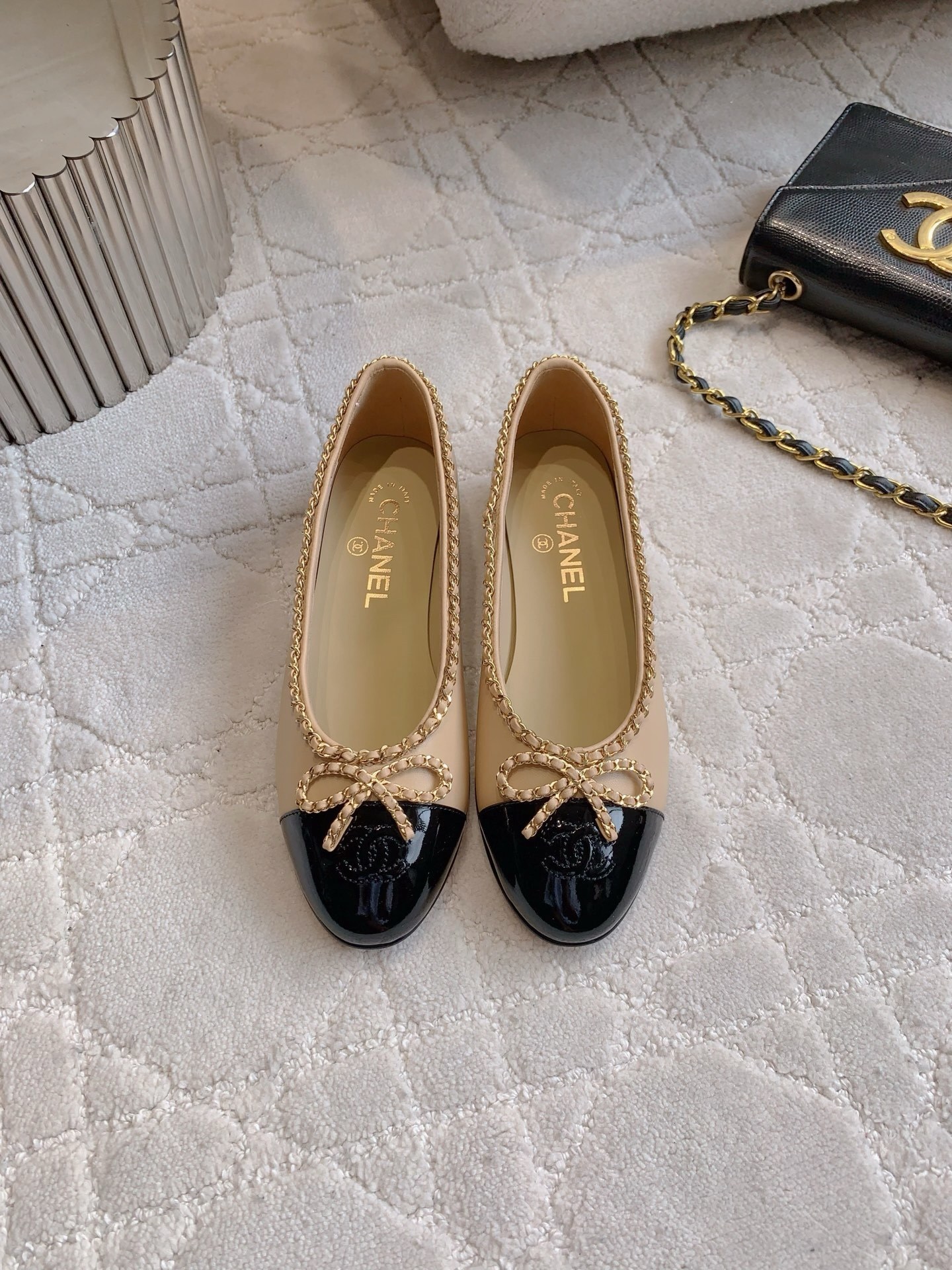 Luxury Chanel beige leather ballerina flats with black patent leather cap toe and gold chain trim detail displayed on a marble surface - Hình 2