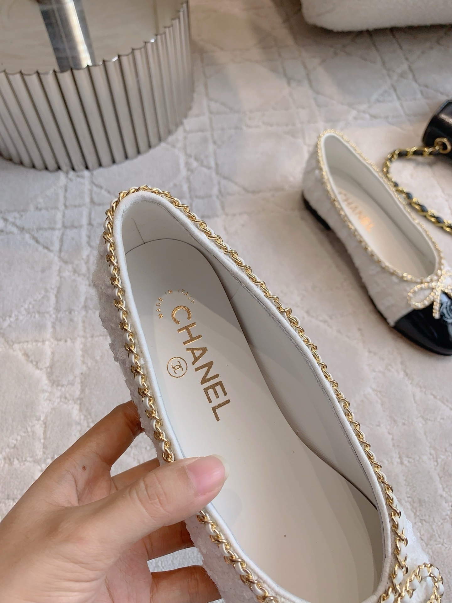Pair of Chanel white tweed ballet flats with black patent leather cap toes and gold chain bow detailing on a white carpet - Hình 8