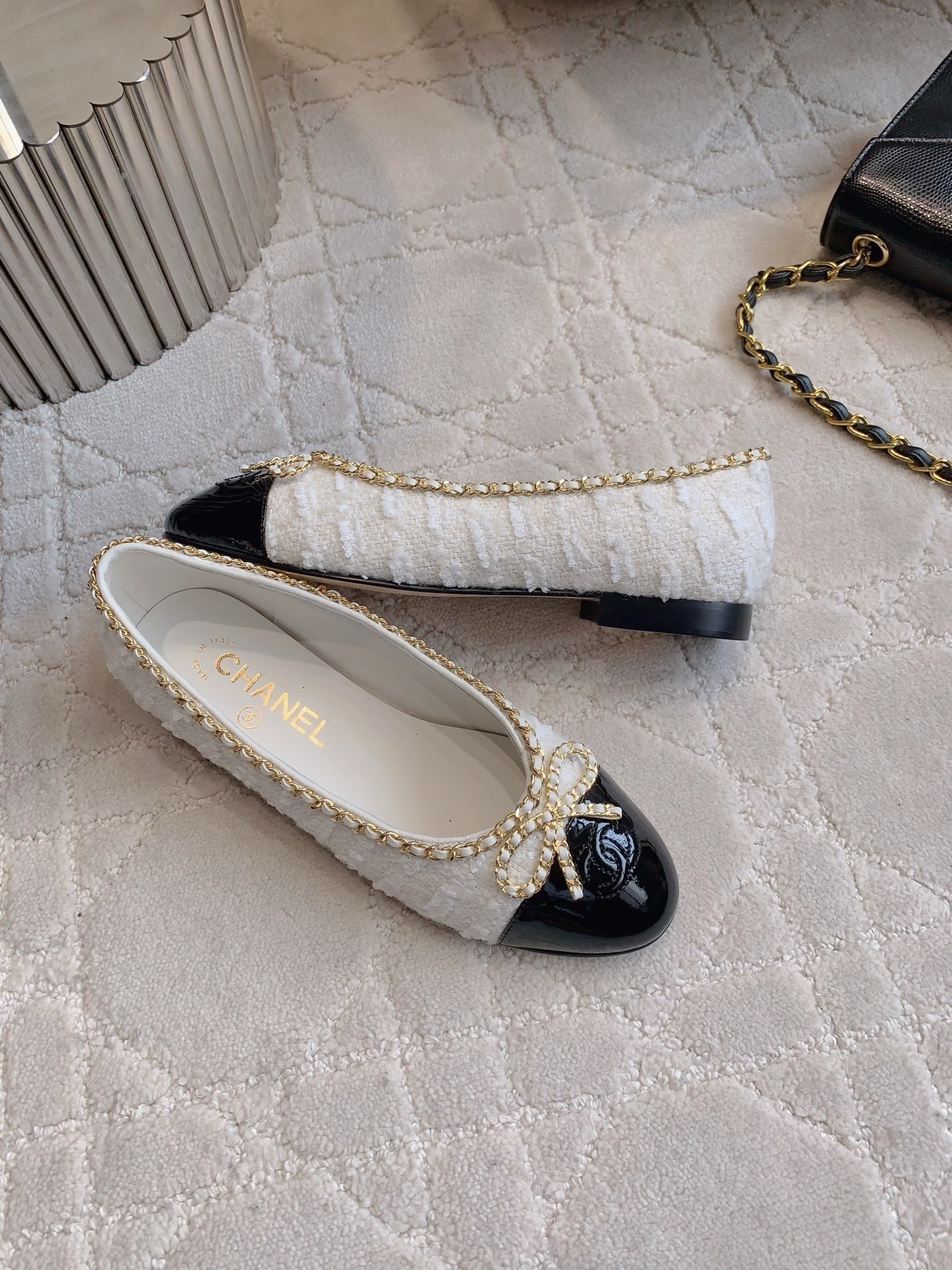 Pair of Chanel white tweed ballet flats with black patent leather cap toes and gold chain bow detailing on a white carpet - Hình 4