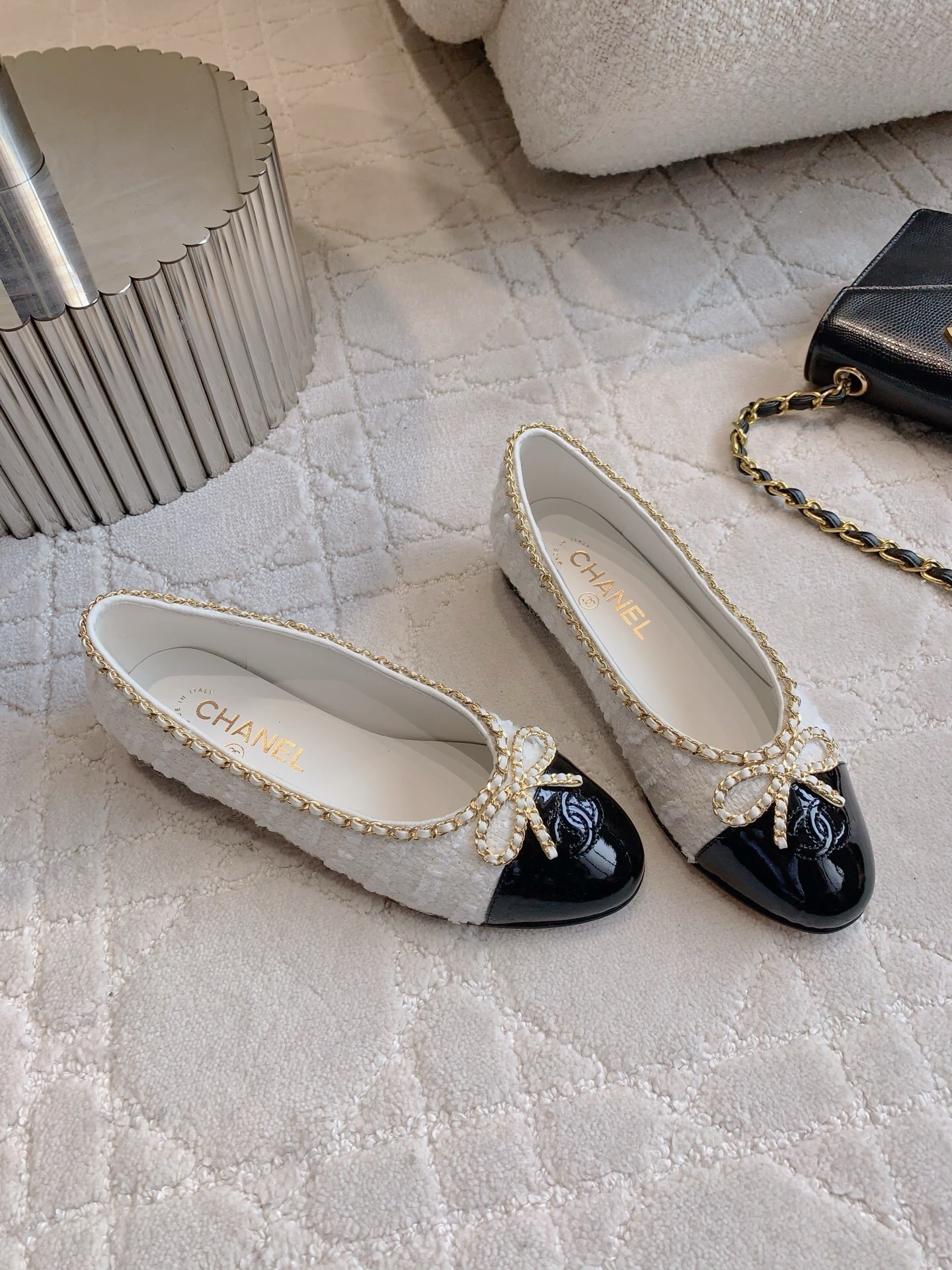 Pair of Chanel white tweed ballet flats with black patent leather cap toes and gold chain bow detailing on a white carpet - Hình 3
