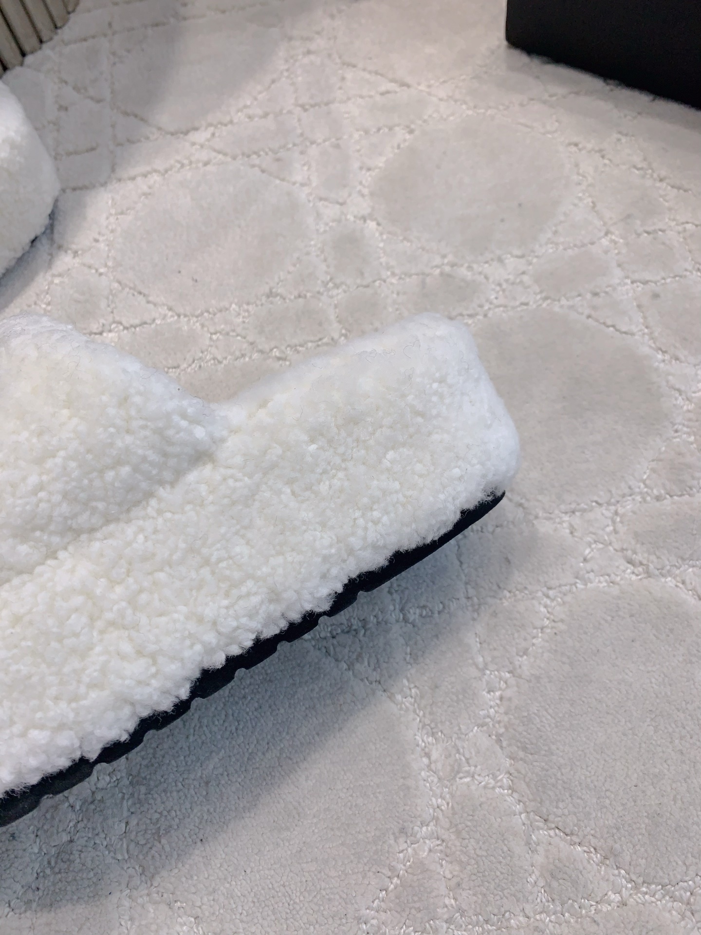 Pair of white fuzzy platform slides with black interlocking logo on a marble table and carpet - Hình 9