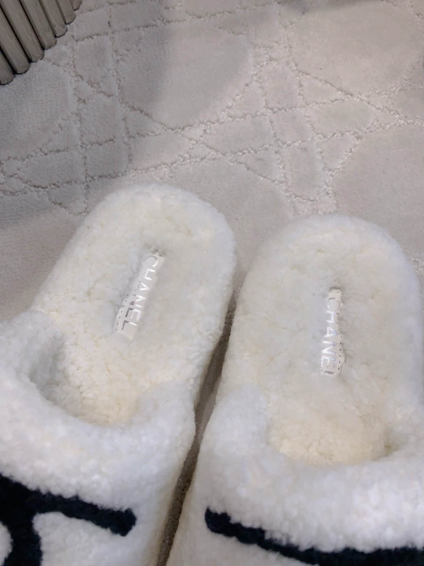 Pair of white fuzzy platform slides with black interlocking logo on a marble table and carpet - Hình 8