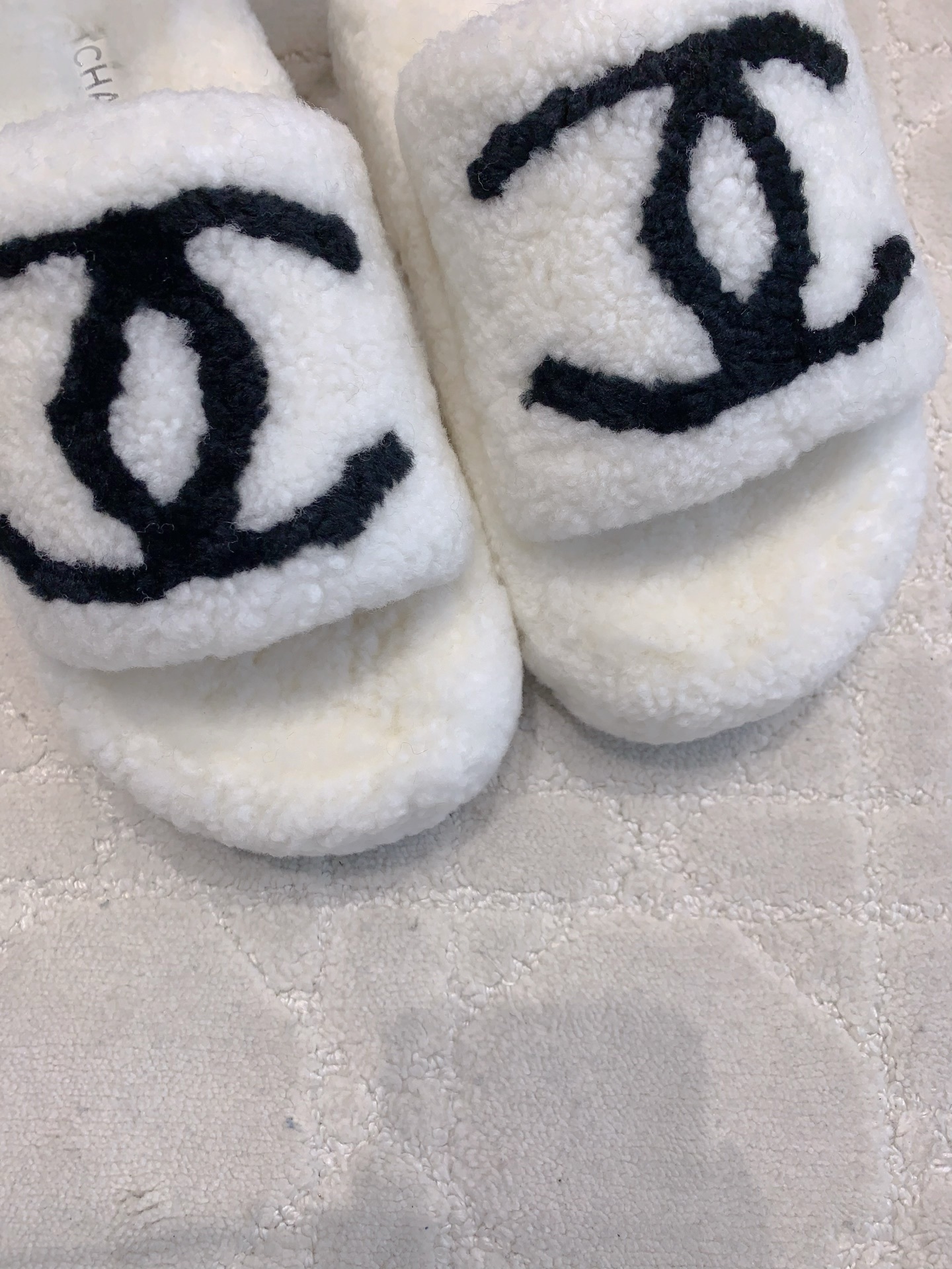 Pair of white fuzzy platform slides with black interlocking logo on a marble table and carpet - Hình 7