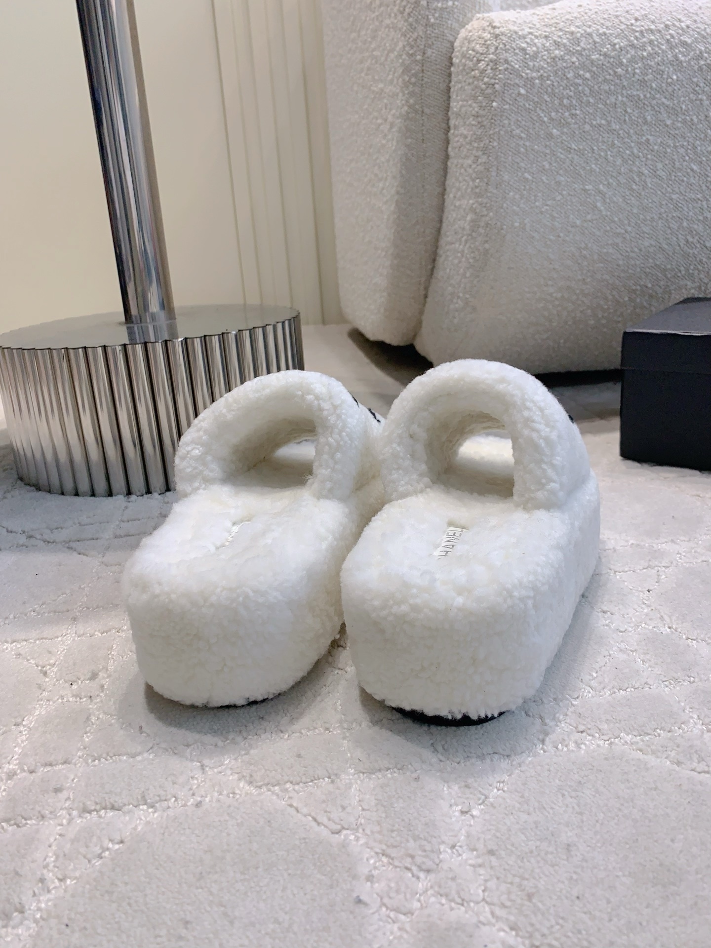 Pair of white fuzzy platform slides with black interlocking logo on a marble table and carpet - Hình 5