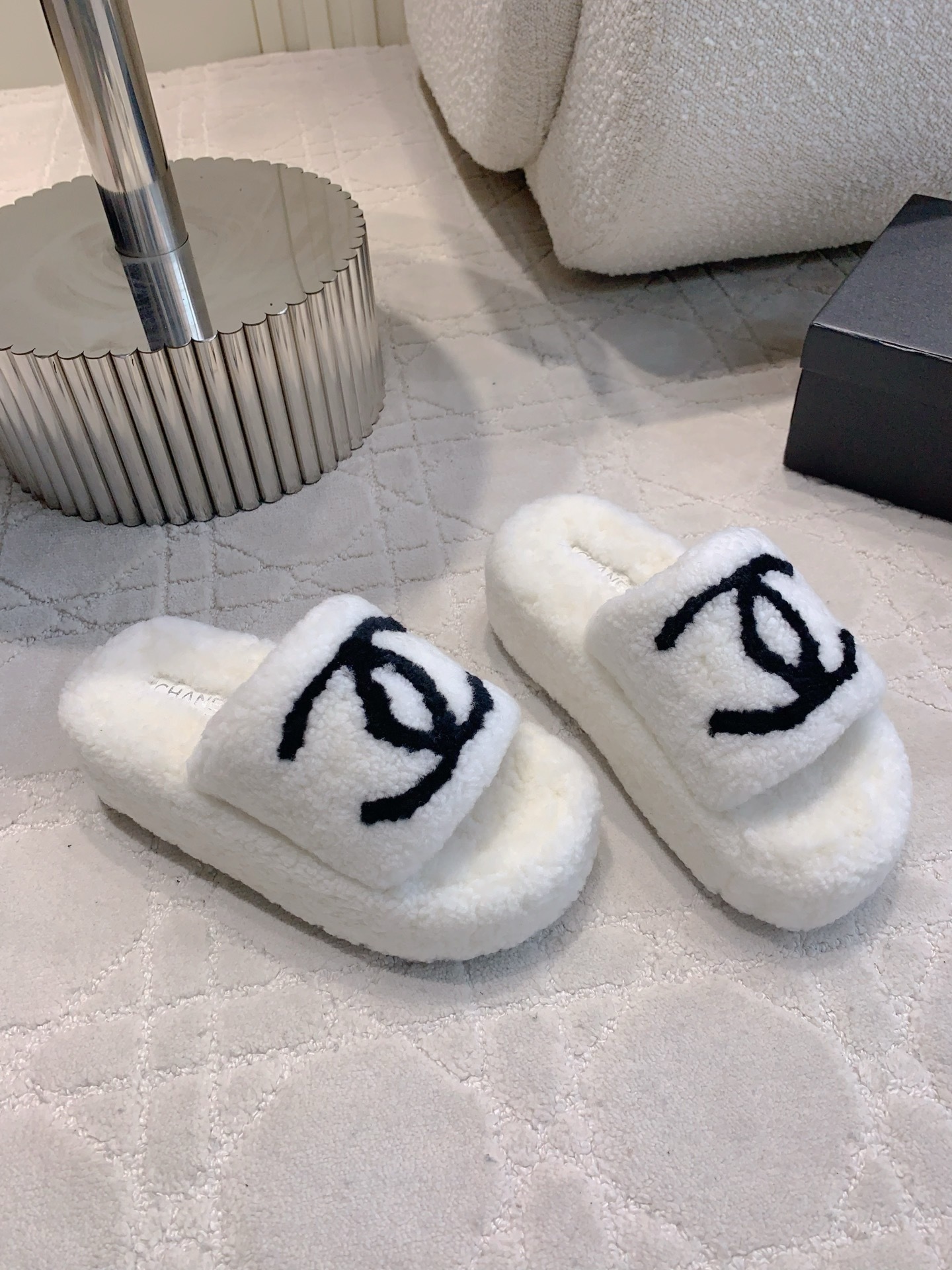 Pair of white fuzzy platform slides with black interlocking logo on a marble table and carpet - Hình 3