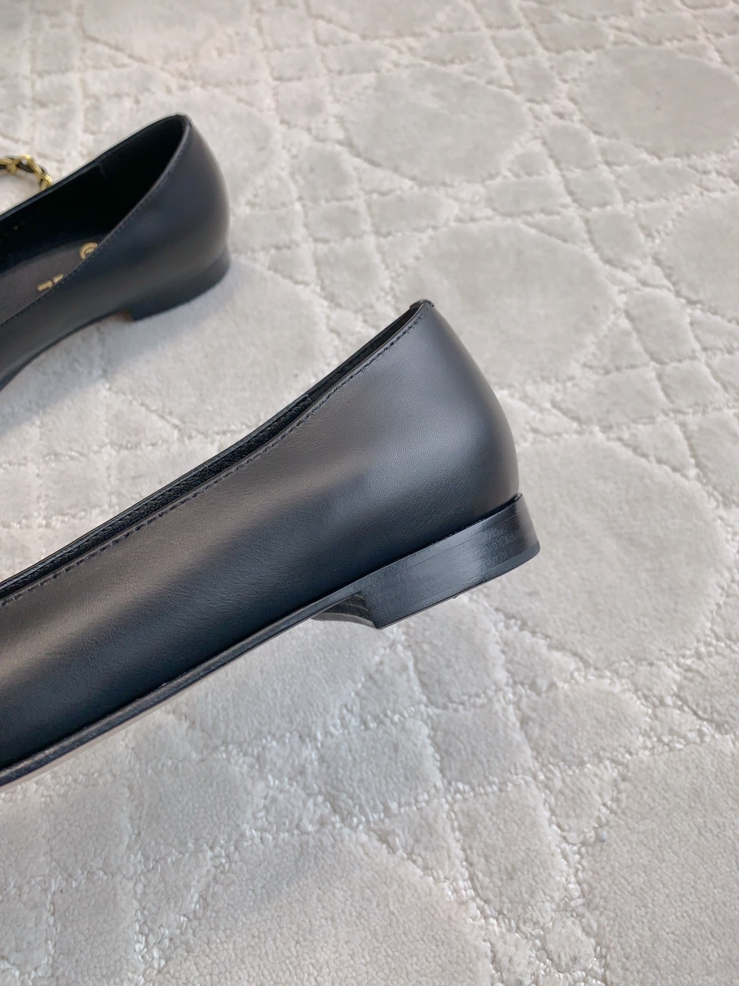 A pair of Chanel black leather ballerina flats with gold chain and CC logo charm displayed on a marble table. - Hình 9