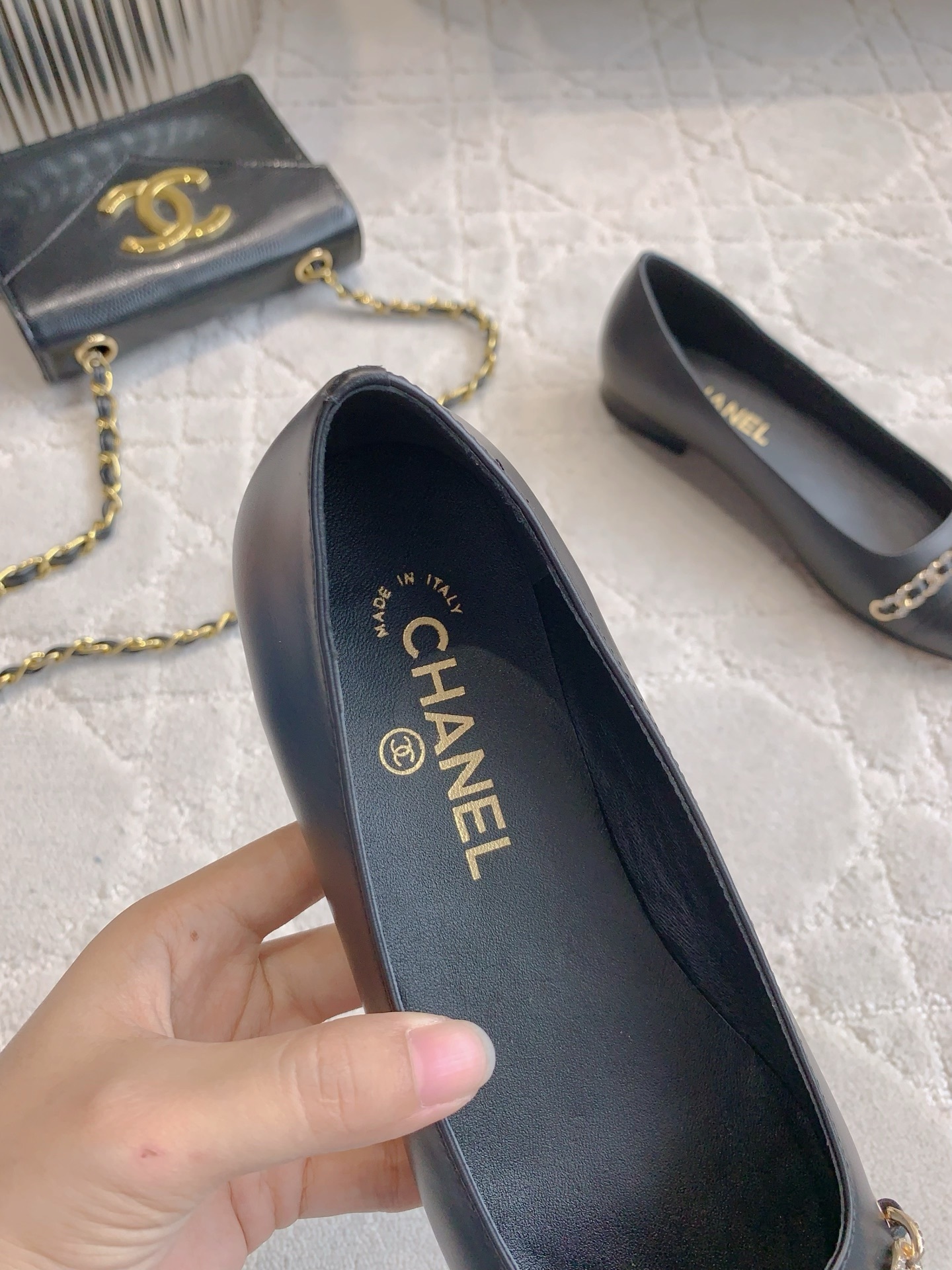 A pair of Chanel black leather ballerina flats with gold chain and CC logo charm displayed on a marble table. - Hình 8