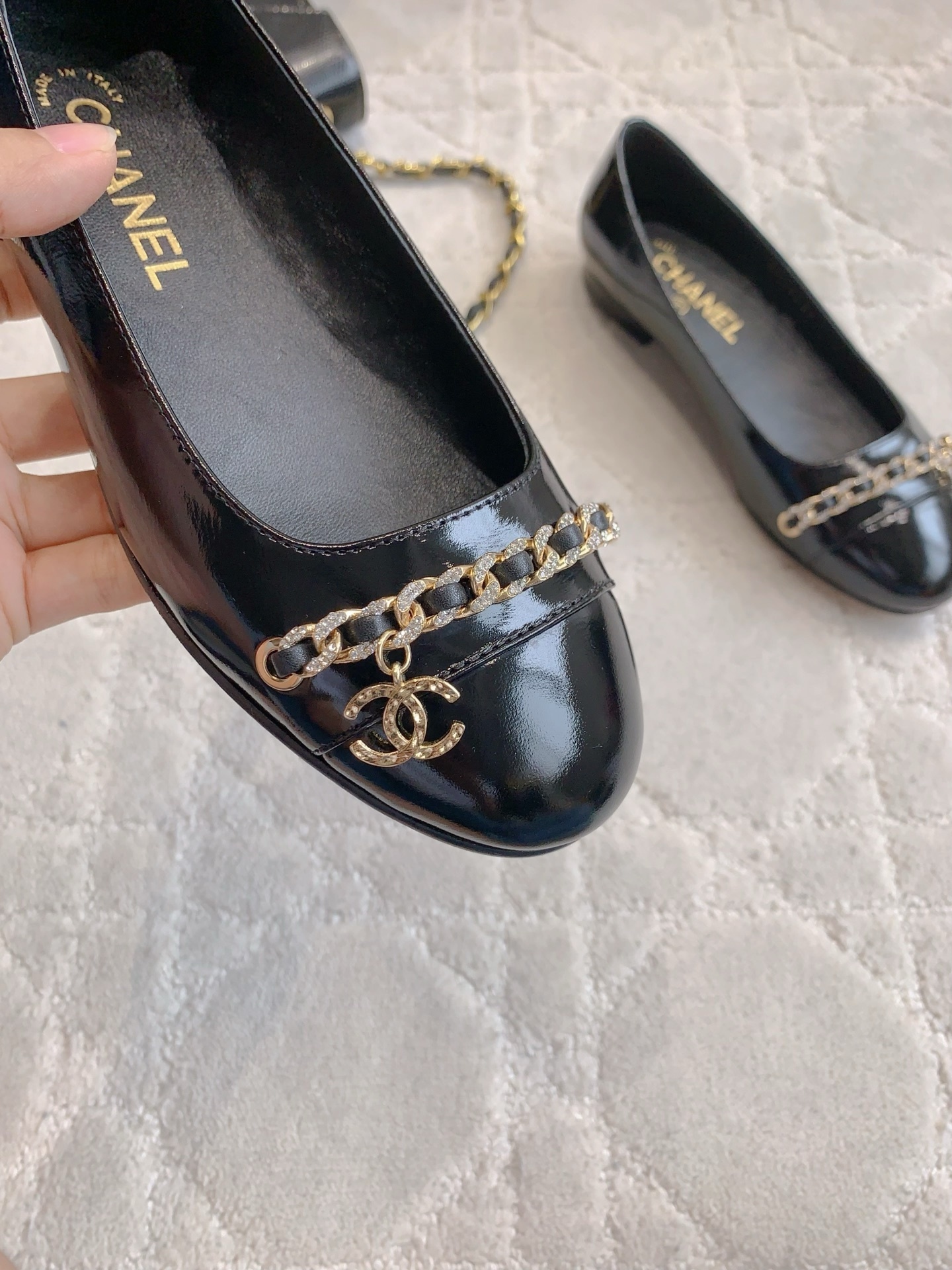 Pair of black Chanel patent leather ballet flats with gold chain and CC logo detailing on a marble surface - Hình 7