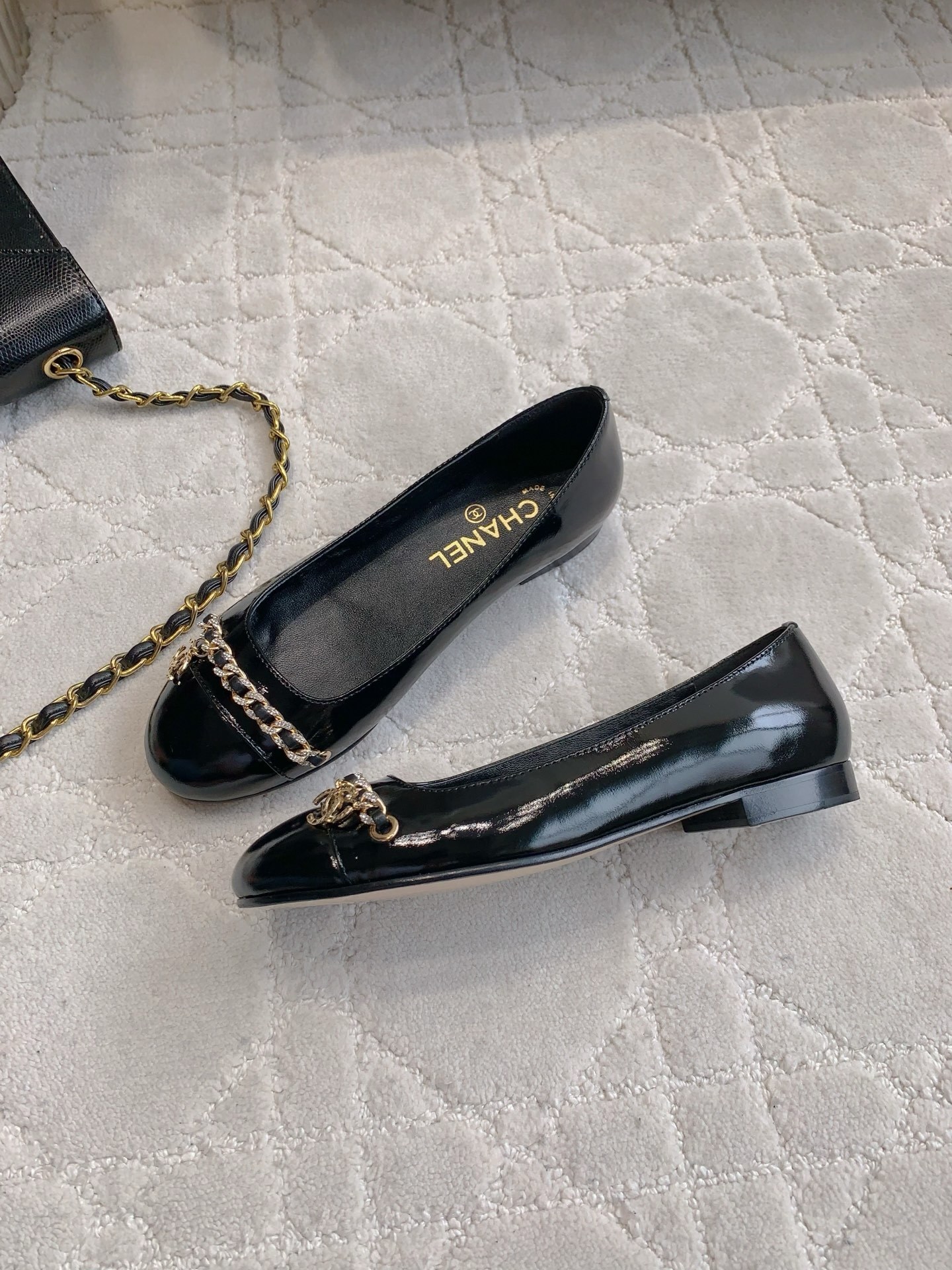 Pair of black Chanel patent leather ballet flats with gold chain and CC logo detailing on a marble surface - Hình 4
