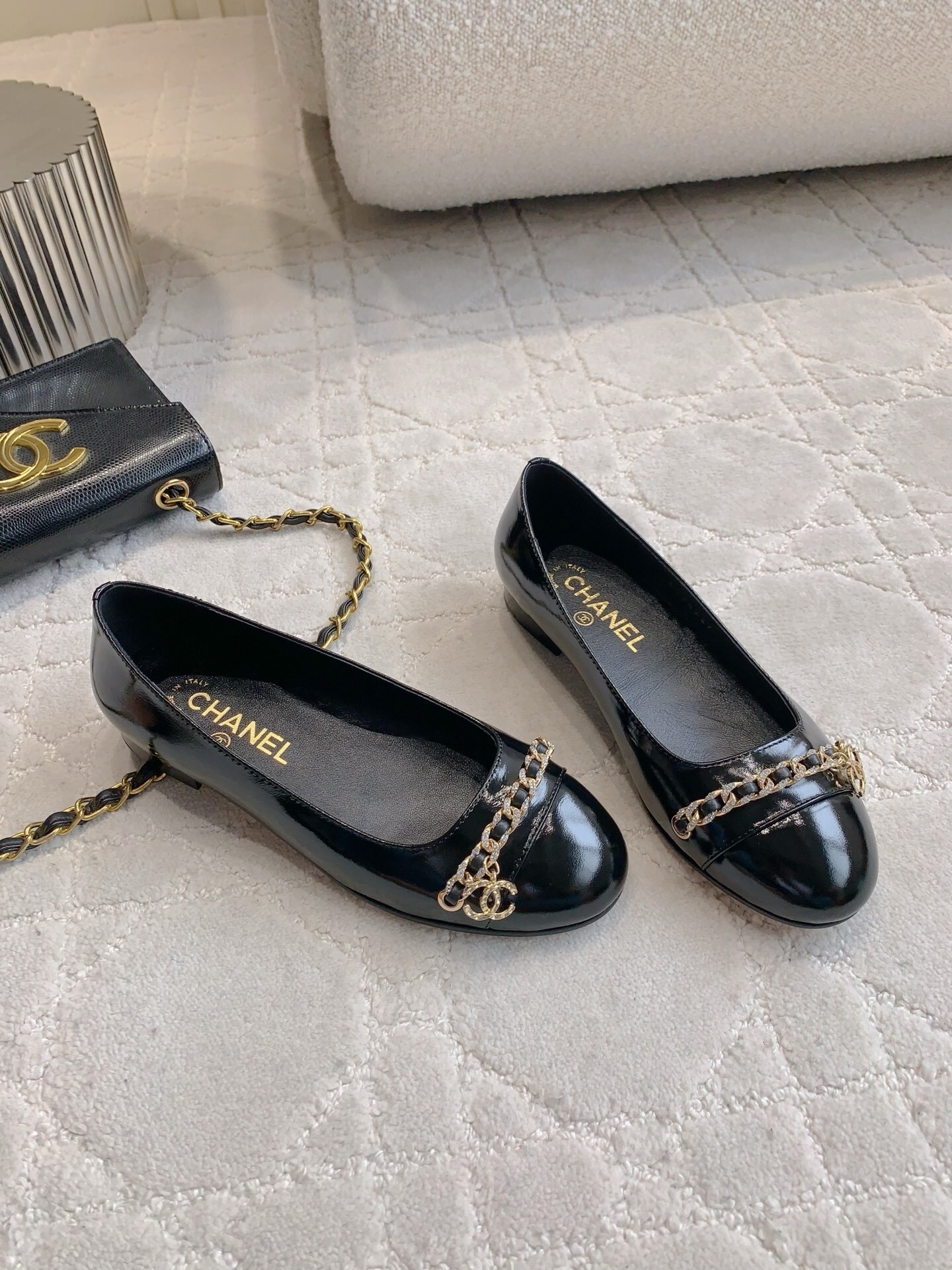 Pair of black Chanel patent leather ballet flats with gold chain and CC logo detailing on a marble surface - Hình 3