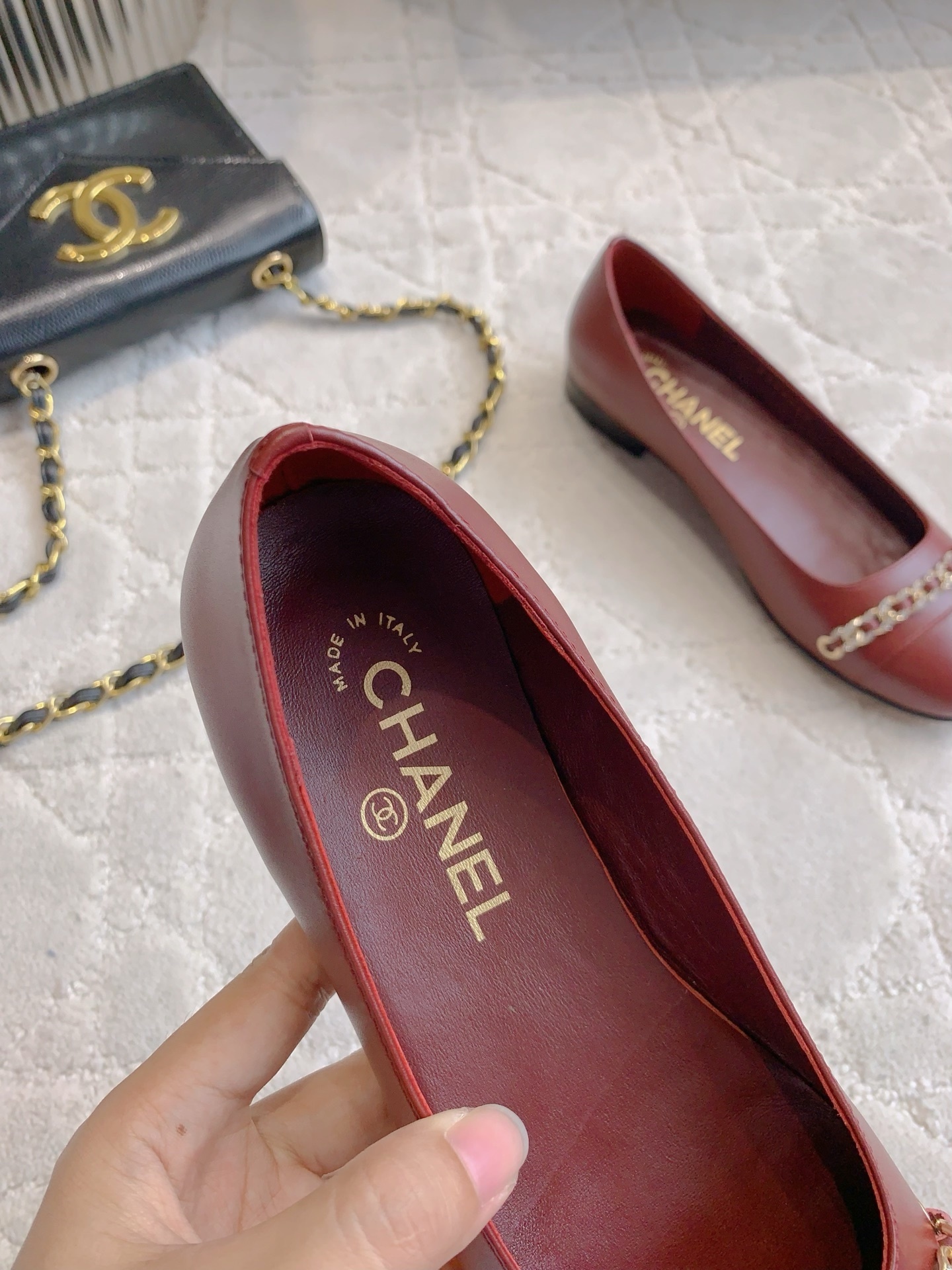 Luxury burgundy red Chanel leather ballet flats with gold chain and CC logo detail on a marble table. - Hình 8
